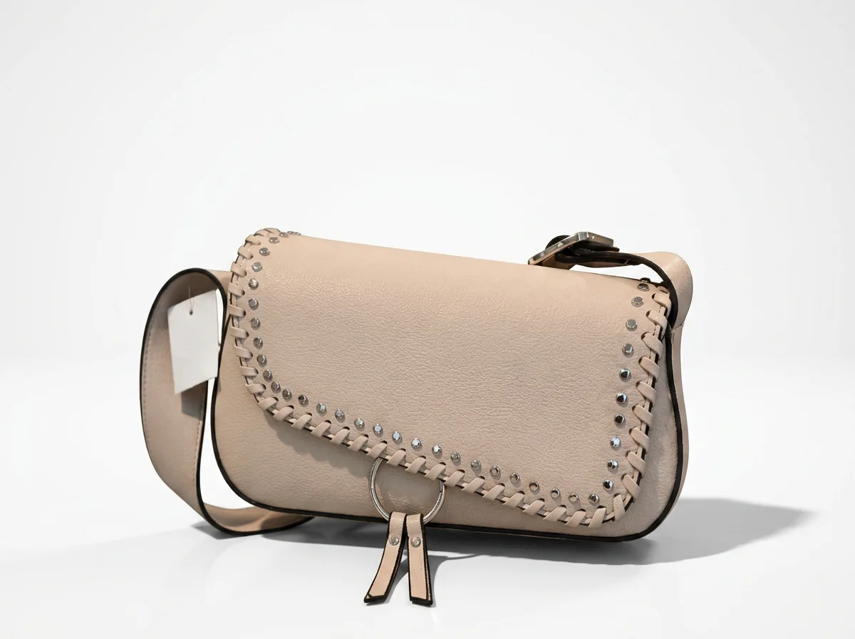 Beige leather handbag with silver studded and braided trim details, placed against a plain white background.