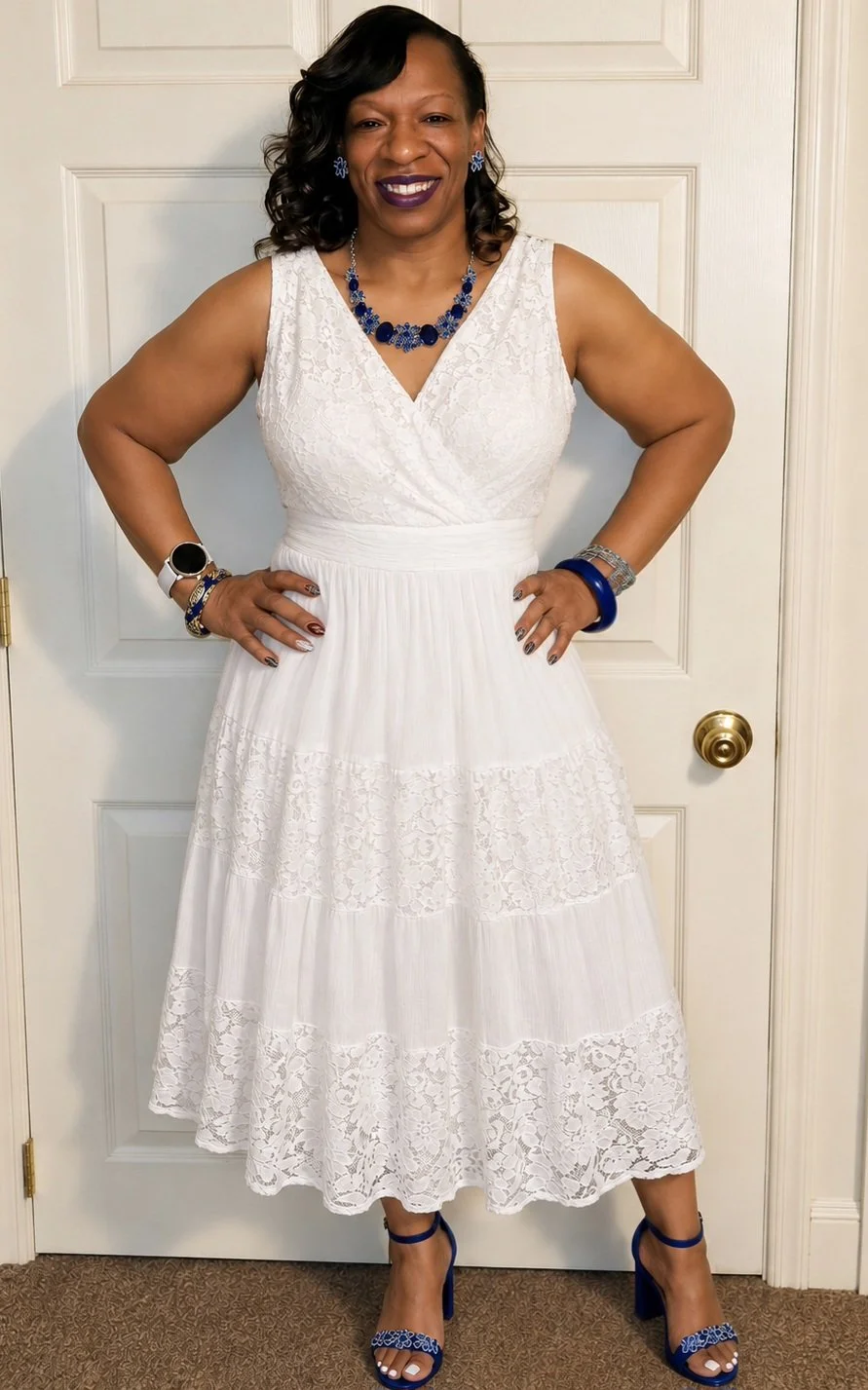 A woman wearing a white lace dress with blue jewelry and matching blue shoes, standing with hands on hips in front of a white door.