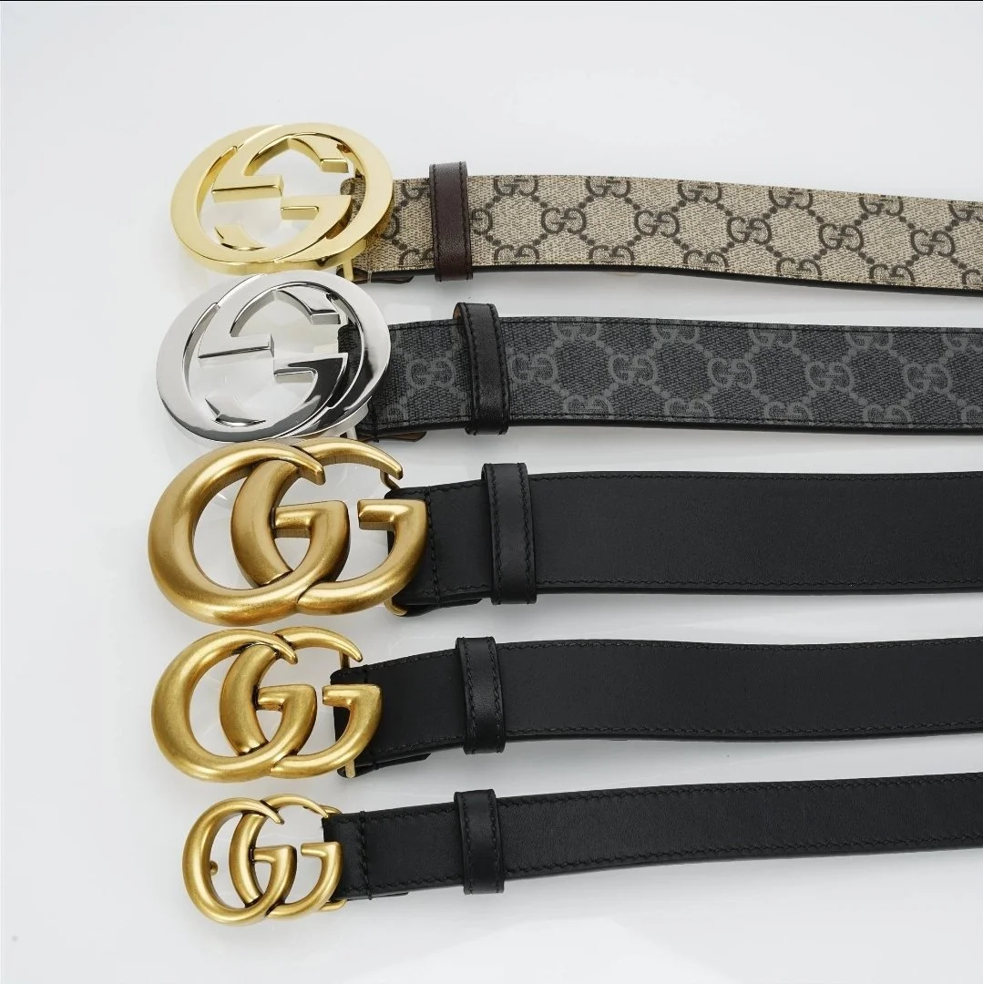 Four designer belts laid out horizontally, with the top belt featuring a beige and brown pattern with Gucci logo, second belt in black and gray with G logo, third and fourth belts in solid black with large and small Gucci G logos in gold.