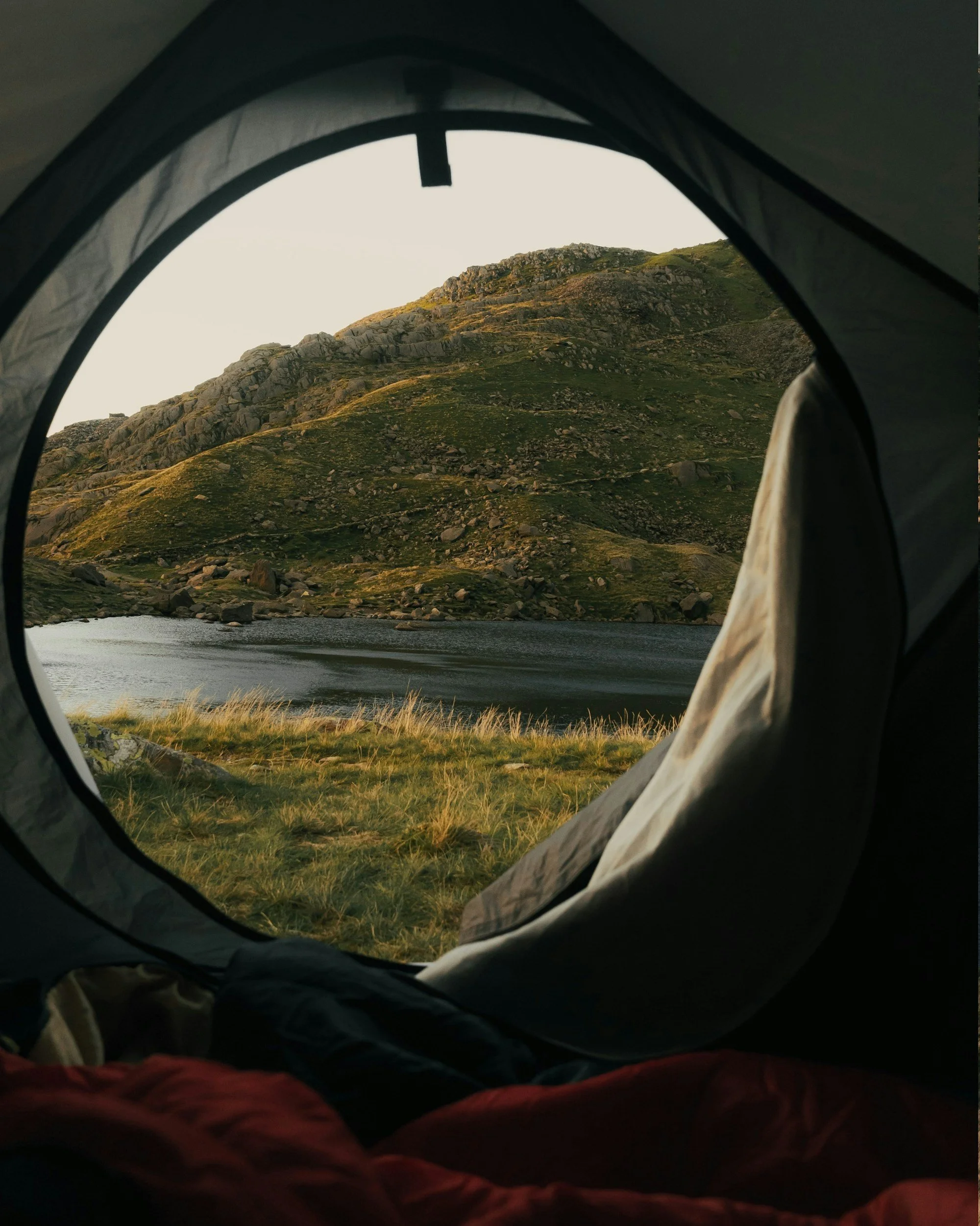 View of a mountain landscape with rocky hills covered in green grass, seen through the opening of a tent.