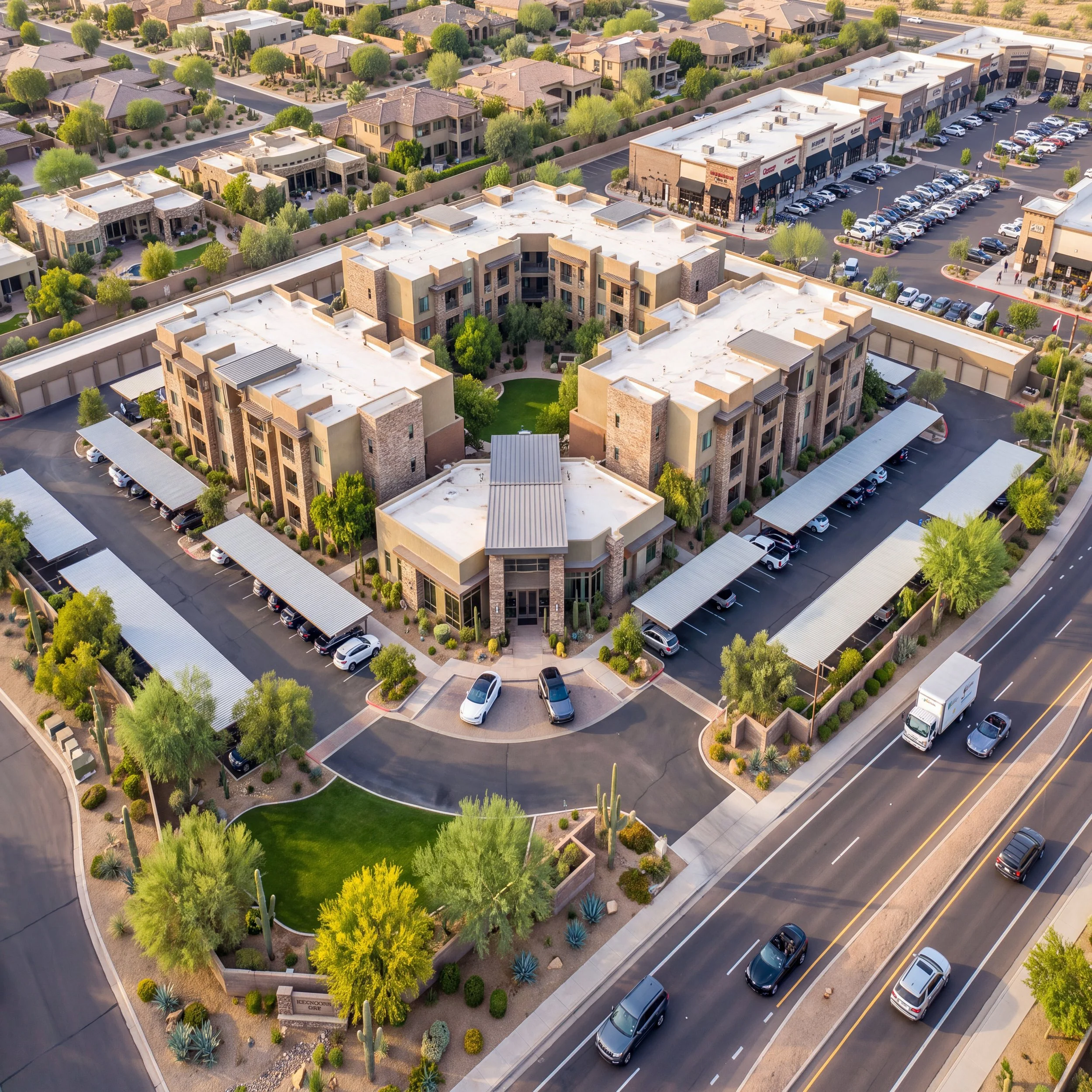 An aerial view of a suburban neighborhood with a mix of residential houses with yards and a shopping center with parking lots filled with cars. The houses are surrounded by trees and greenery, and there's a main road with cars driving by.