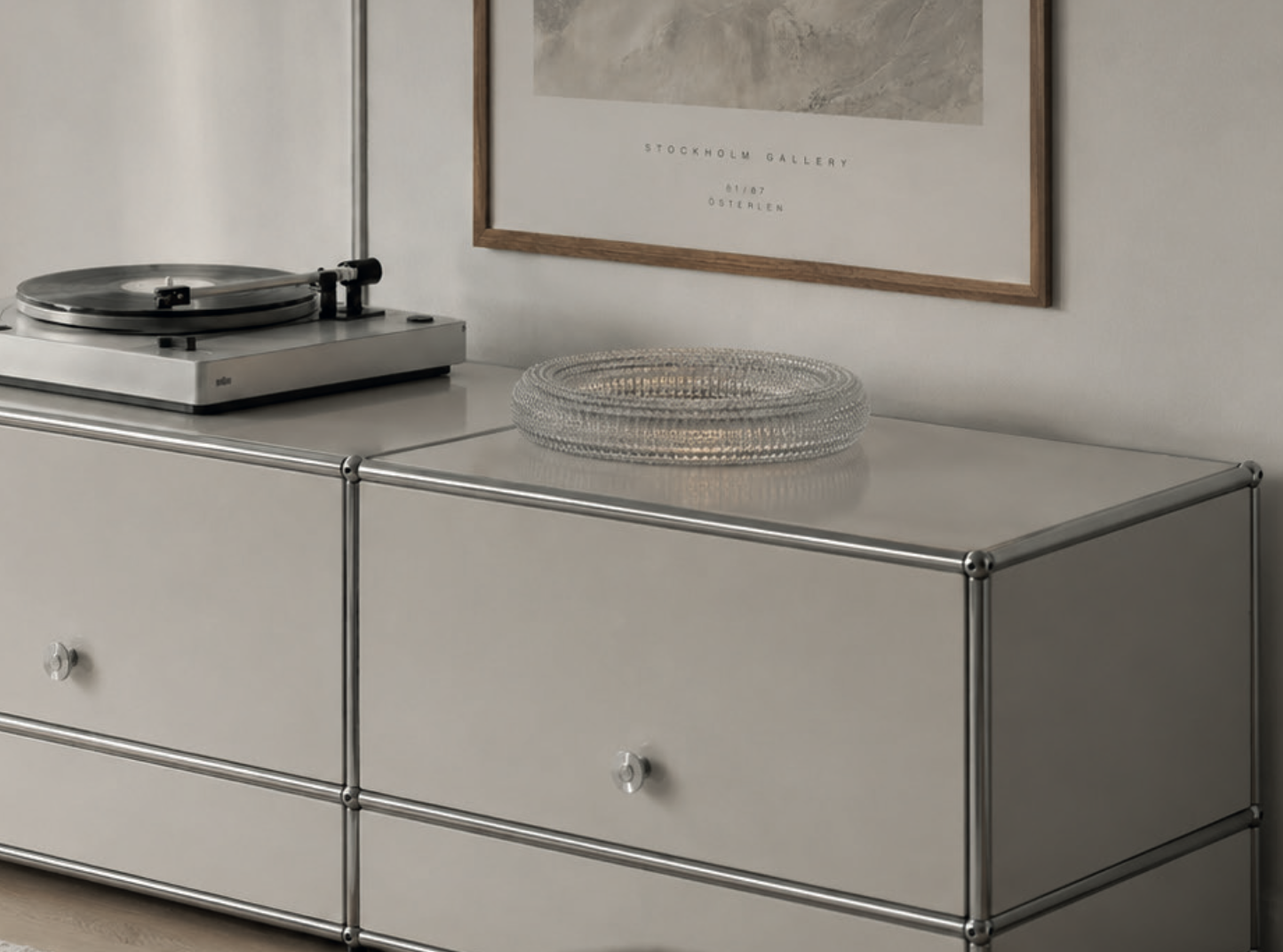 En hvit møbeltopp med metallramme, med en plate på toppen. På toppen står en platespiller og en klar glassfat.