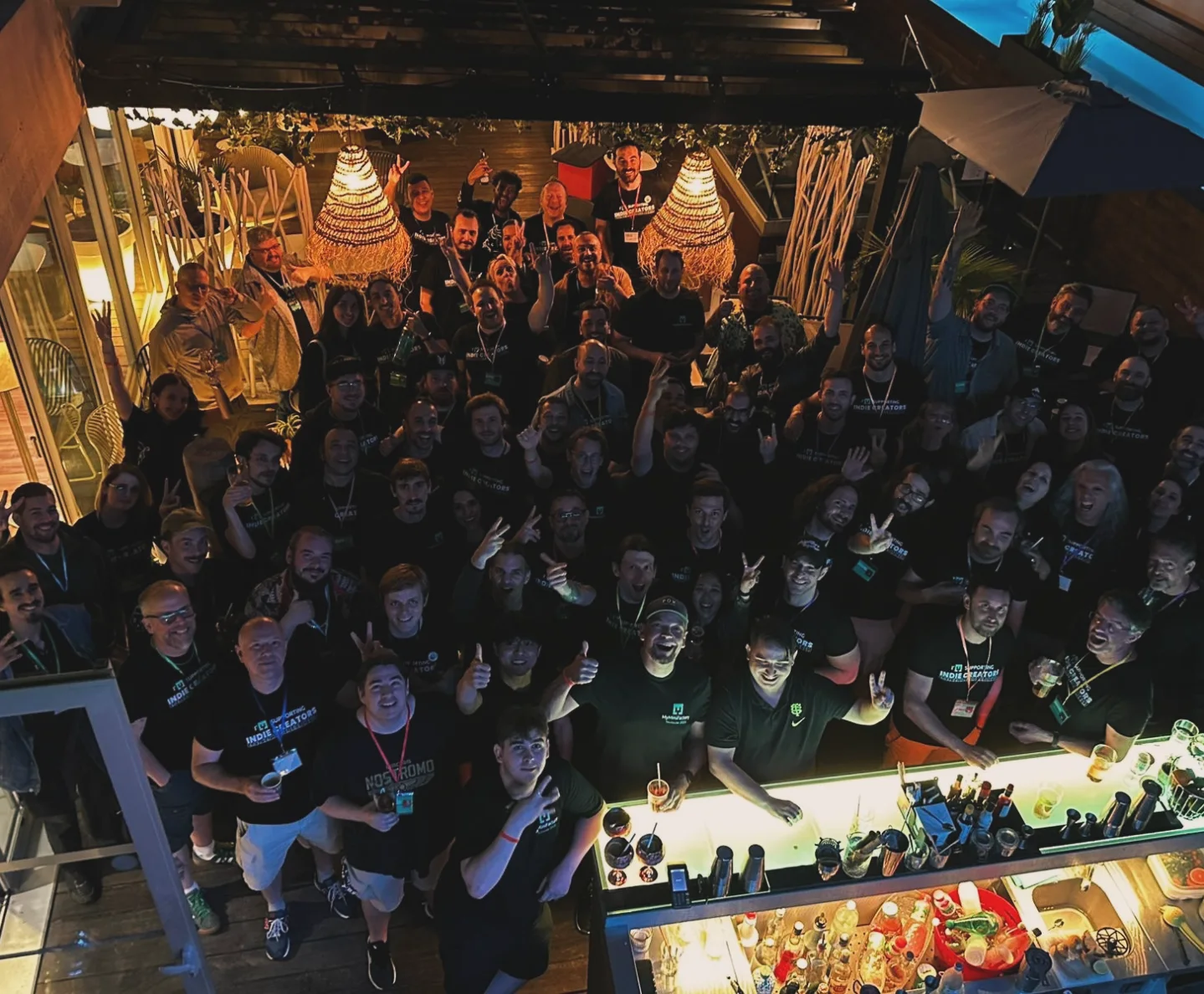 Group of people celebrating at a lively social gathering at night, with a bar and warm lighting.