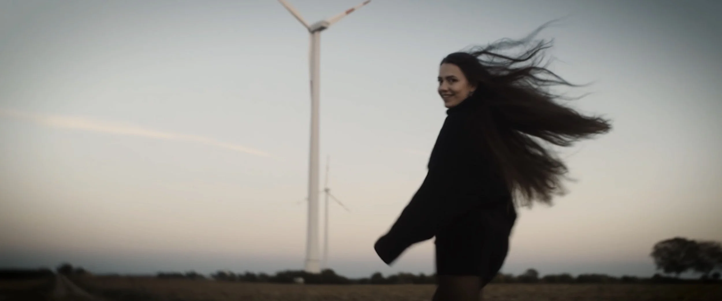 Cinematic Video A laughing woman with long brown hair blowing in the wind stands in an open landscape at sunset.