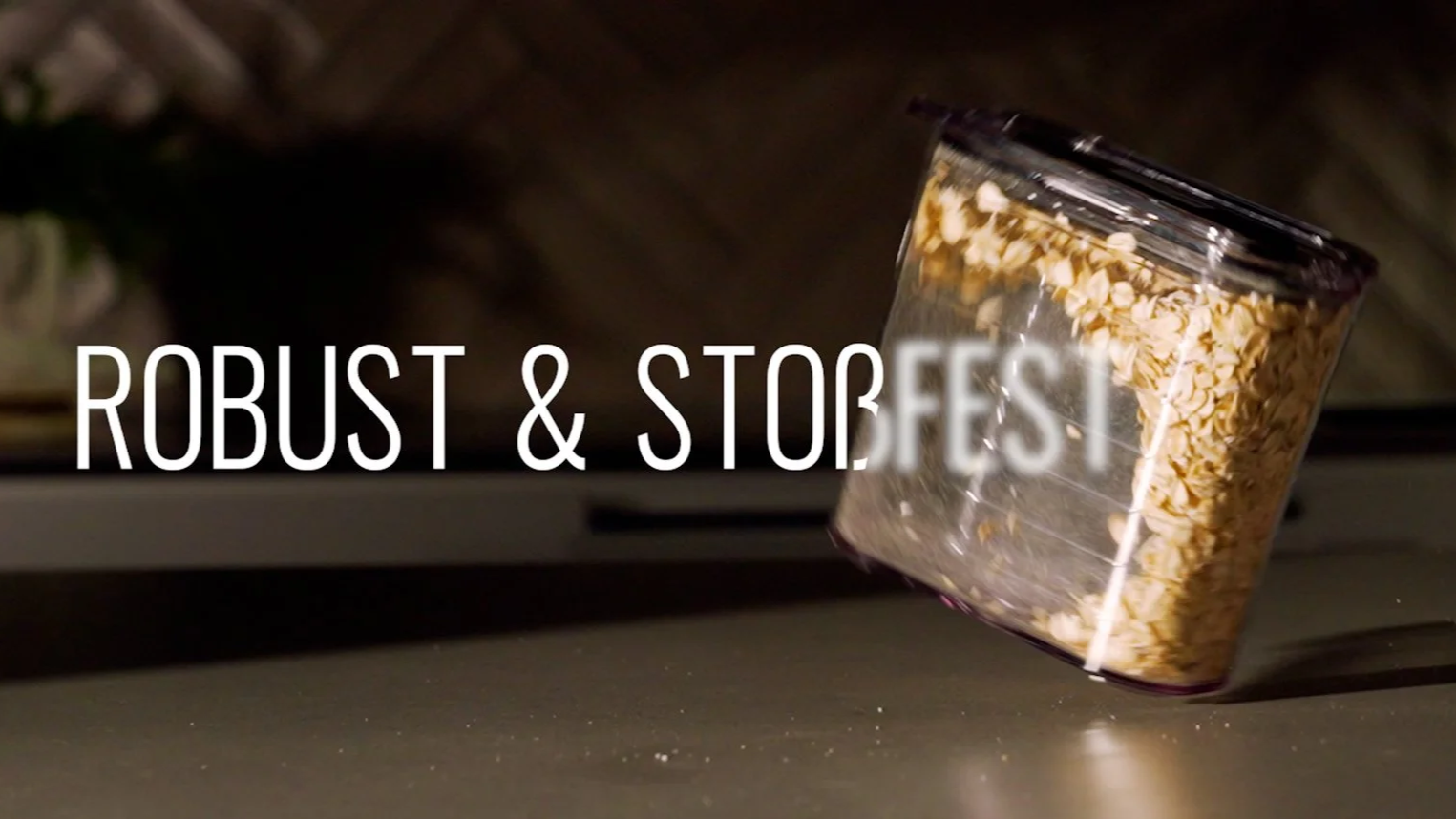 Ein transparentes Glas mit Hafer, das umkippt, auf einer dunklen Oberfläche, mit dem Text 'Robust & Stoßfest' im Vordergrund.