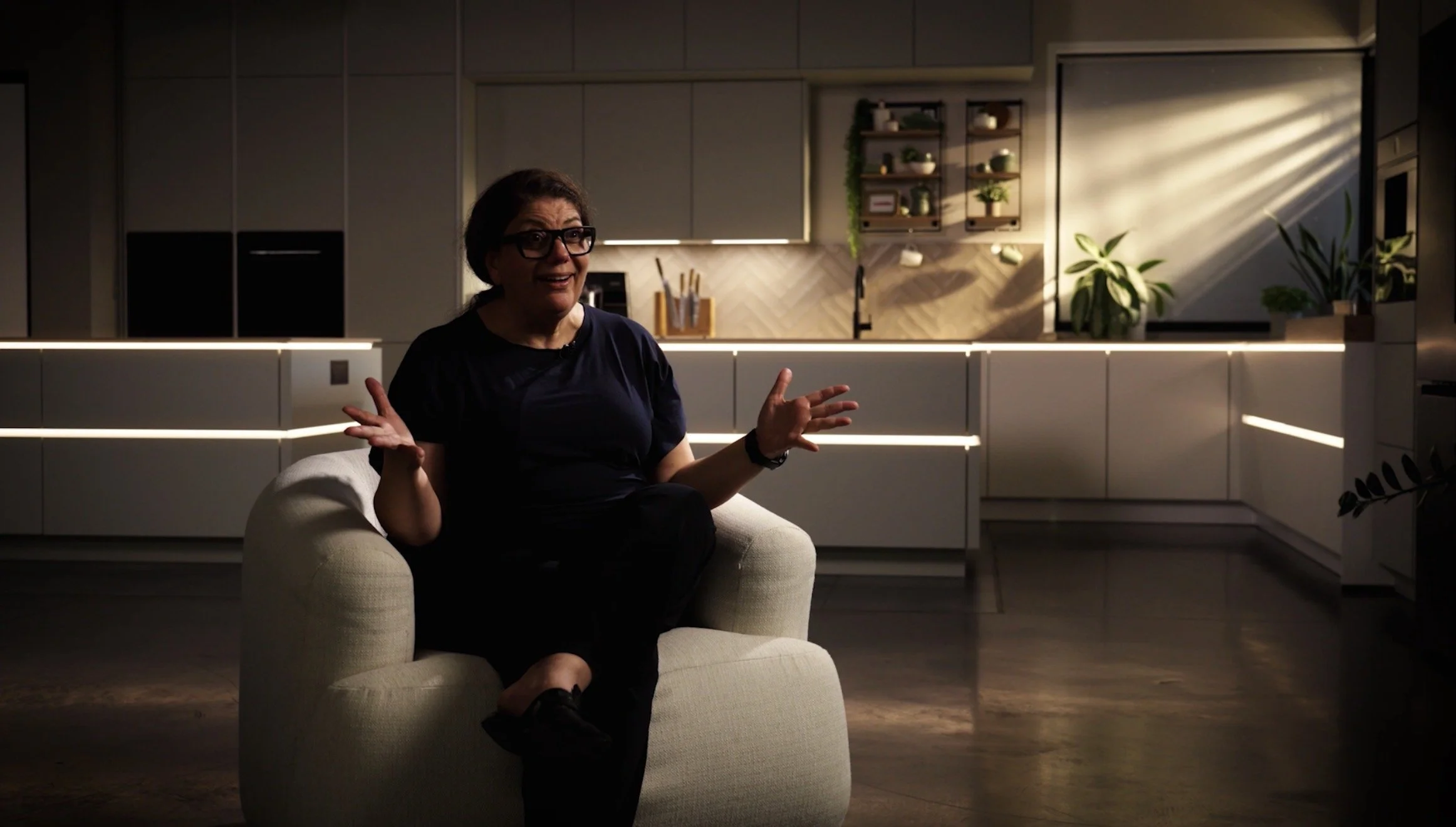 Cinematic Interview, A woman sits on a white sofa in a modern, well-lit kitchen and speaks.