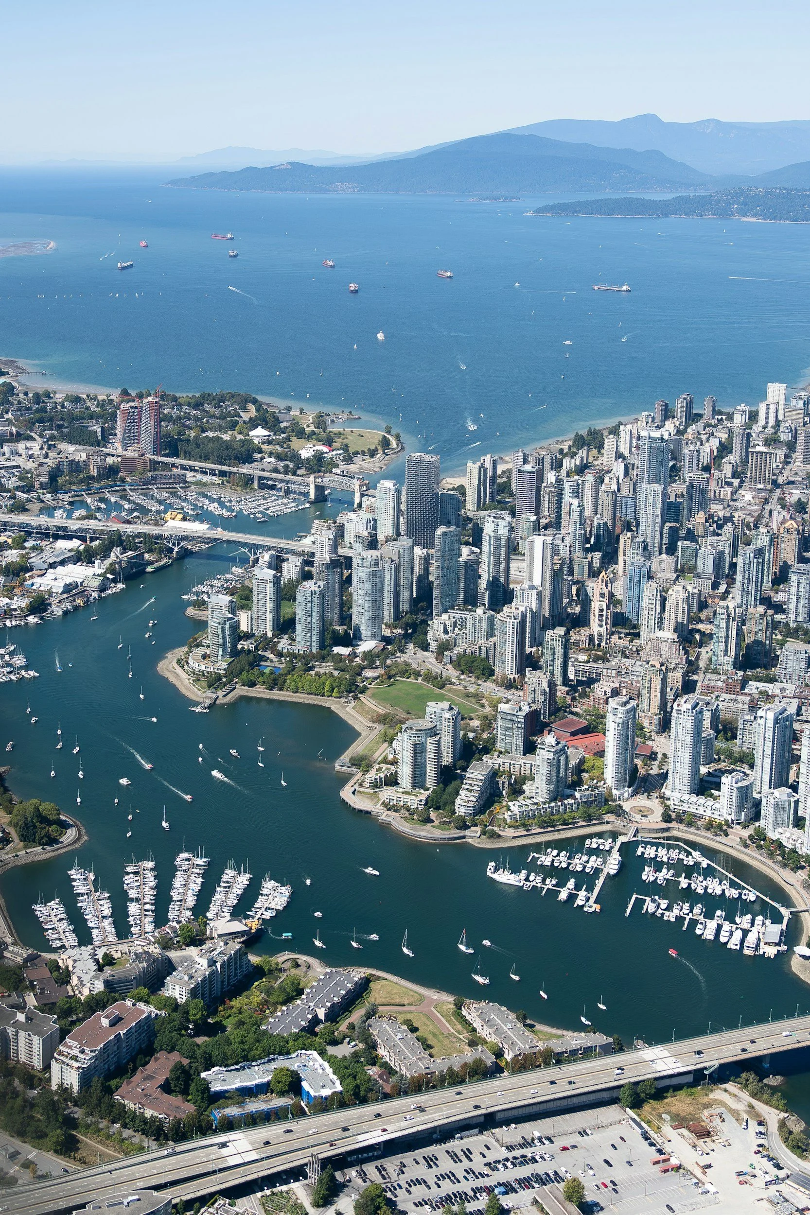 Aerial view of downtown Vancouver, British Columbia, with high-rise buildings, marinas, boats, False Creek, Burrard Inlet, and North Shore mountains.