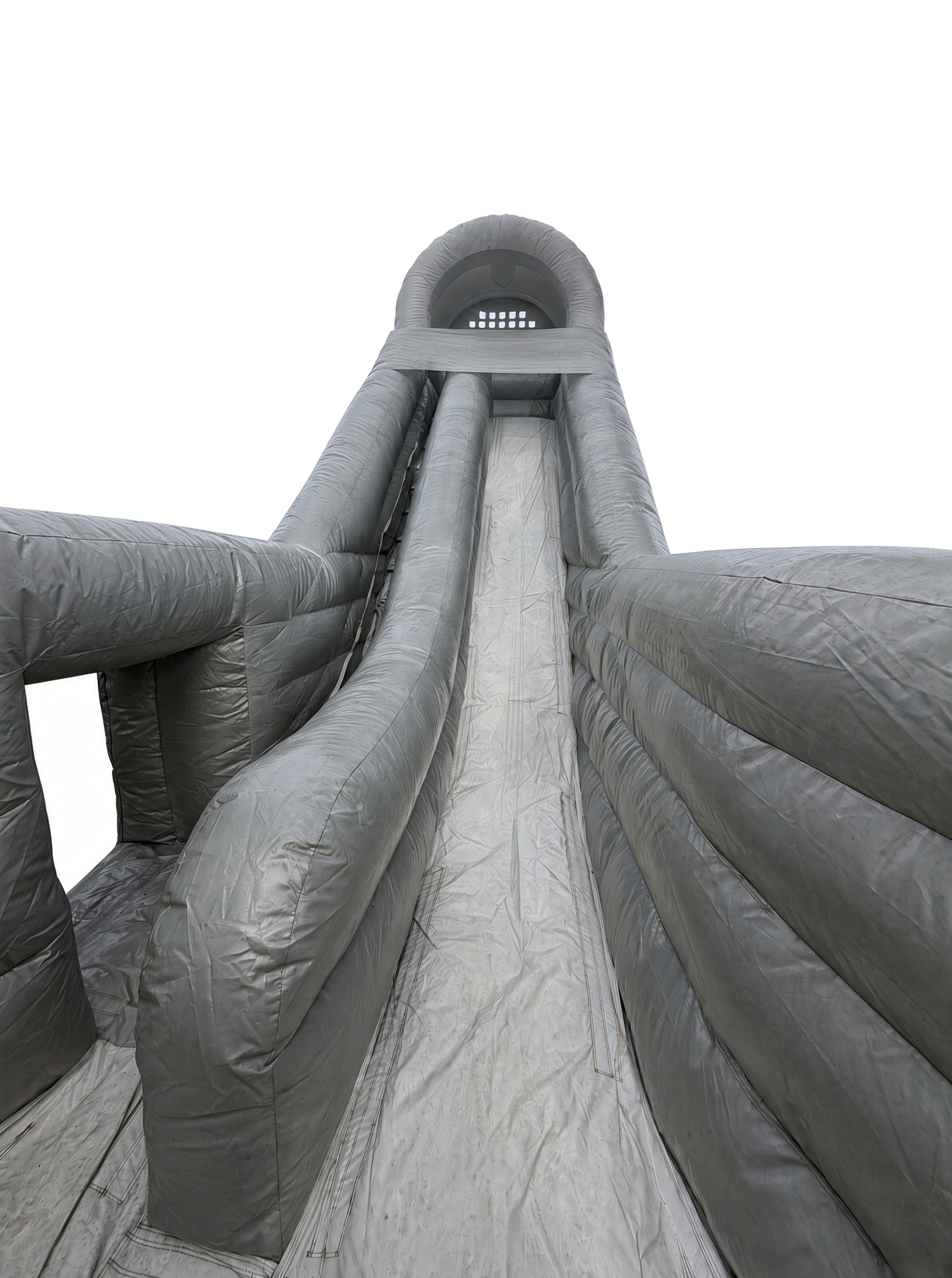 Large outdoor inflatable water slide with multiple sliding lanes seen from the bottom, leading up to a tower with a ladder at the top, against a mostly cloudy sky.