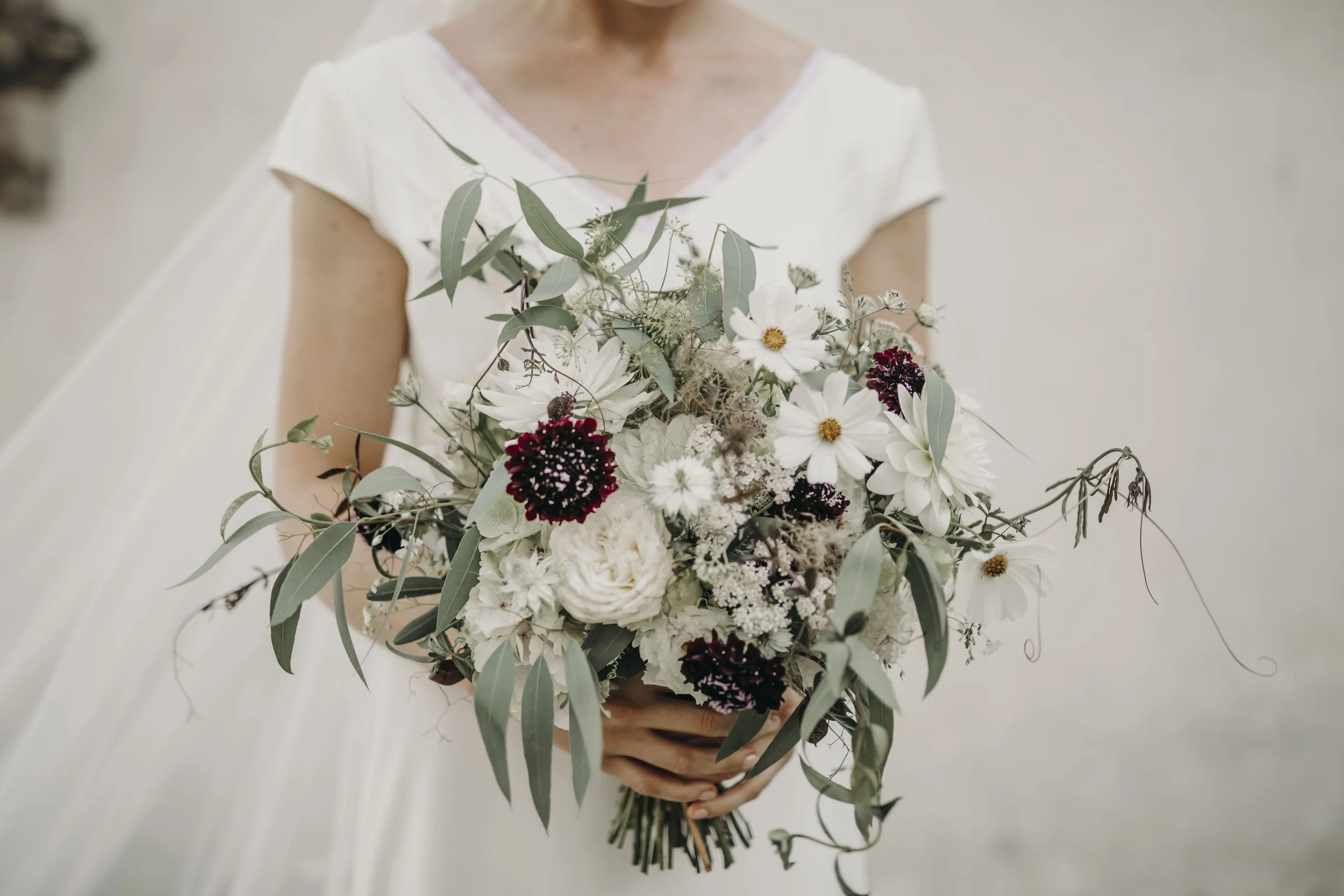 Person holding a bouquet of white, red, and green flowers against a neutral background.