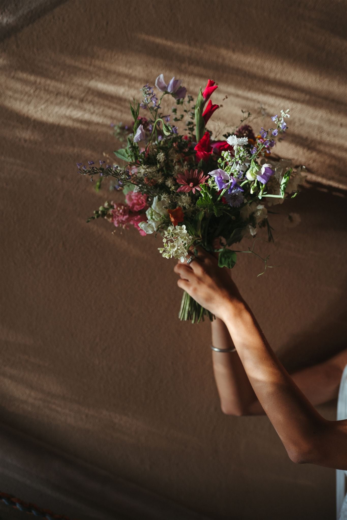 A person holding a colorful bouquet of mixed flowers over a brown couch with a textured fabric.