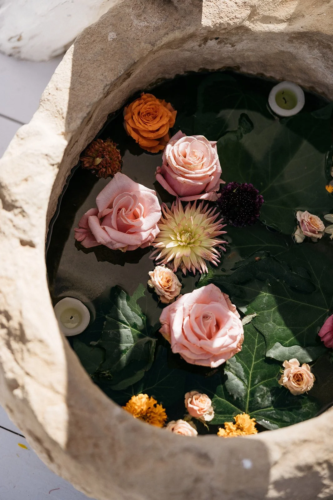 Floating flowers and candles in a stone bowl with water.