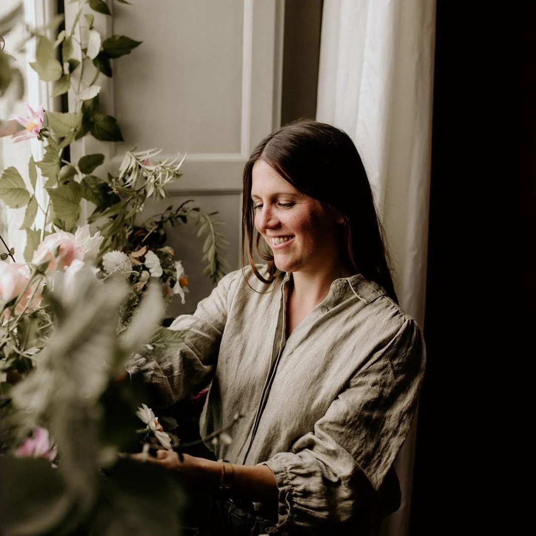 Woman arranging or tending to pink and white flowers in a well-lit room.
