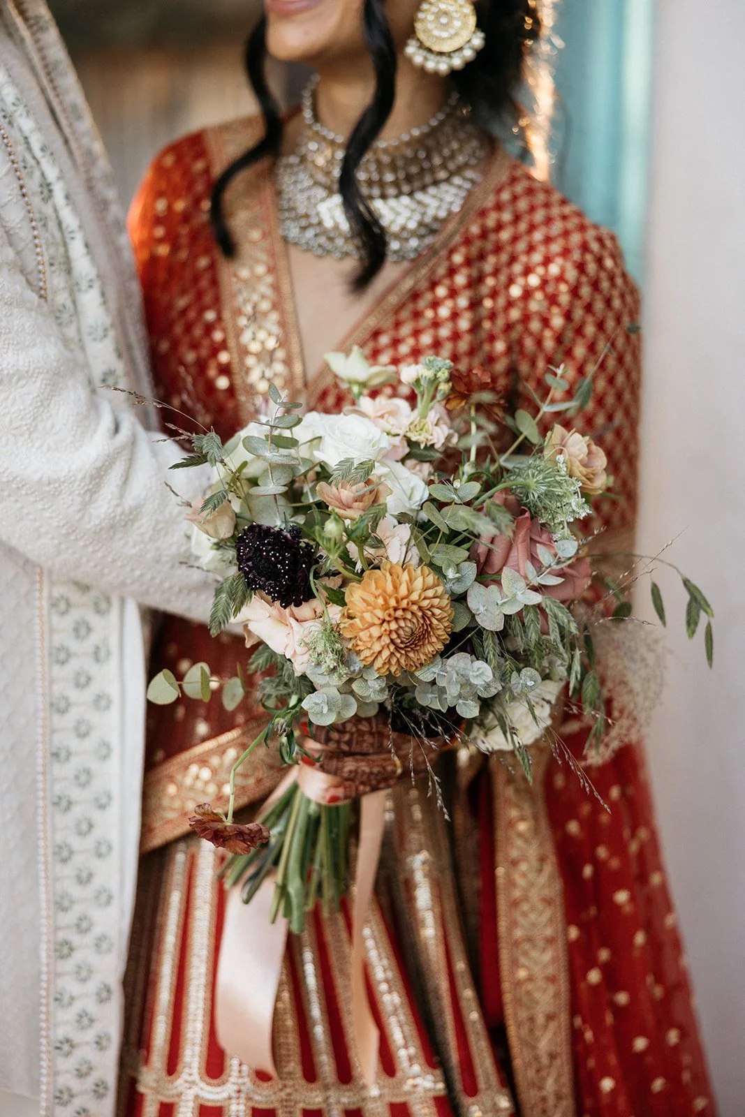 A woman in traditional Indian attire holding a bouquet of mixed flowers with greenery.