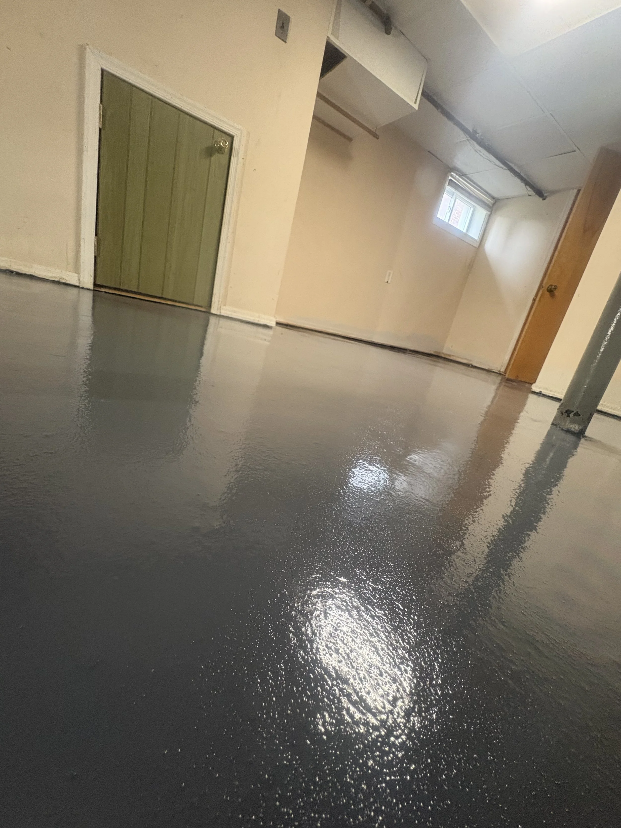 Interior room with unfinished walls, small window, and freshly painted black concrete floor.