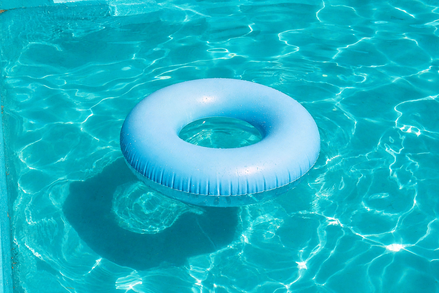 A blue inflatable pool float shaped like a ring floating on the water in a swimming pool.