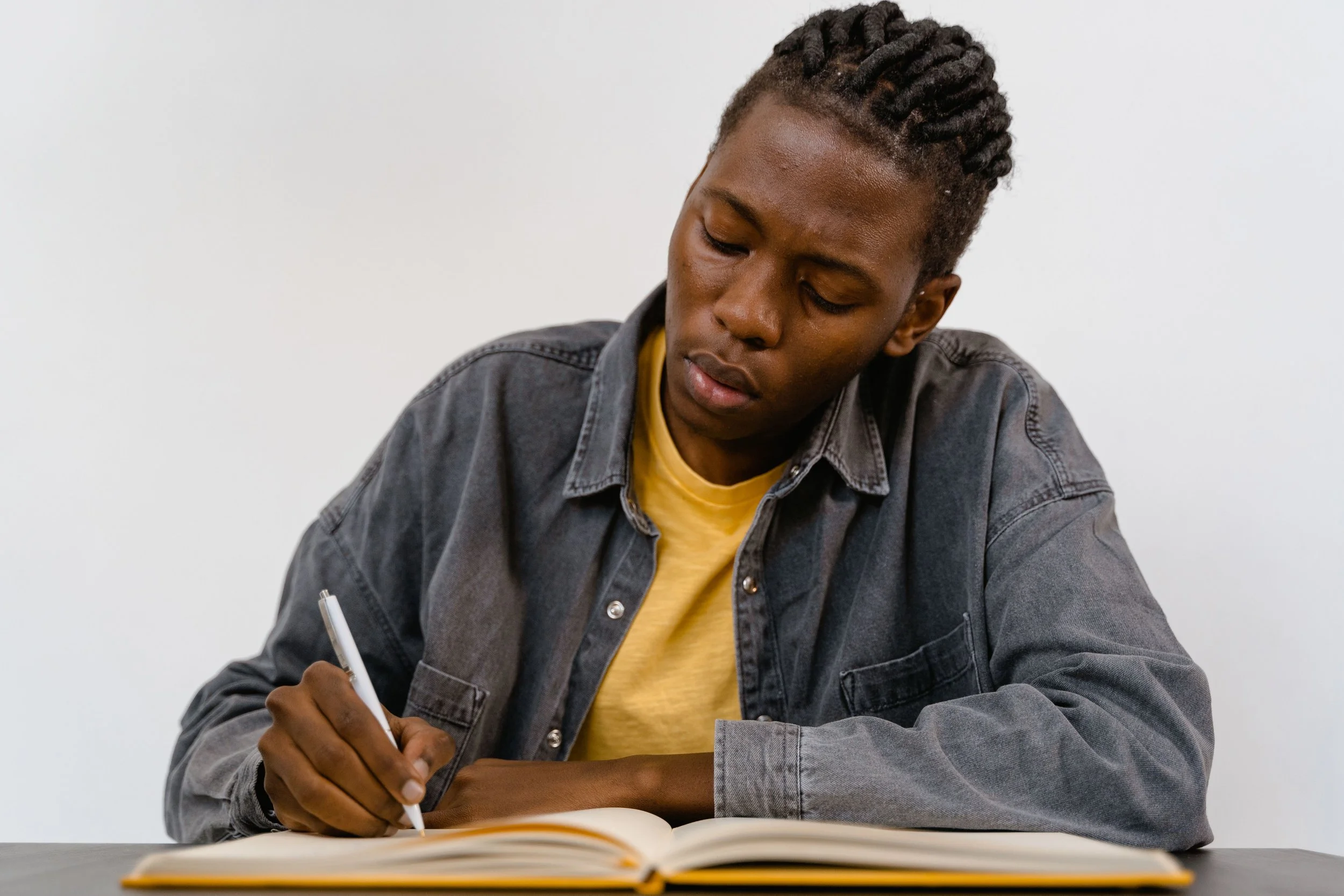 dreadlocks writing intently in a notebook, conveying concentration and creativity.
