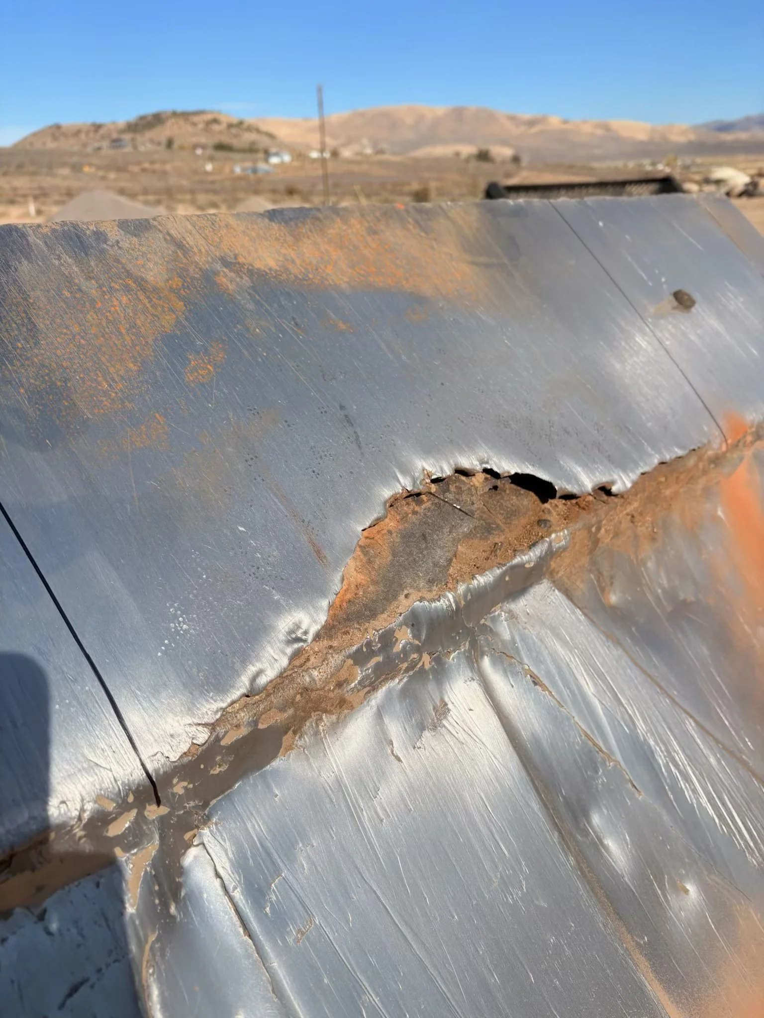 Close-up of a severely rusted and cracked metal vehicle surface with desert hills in the background