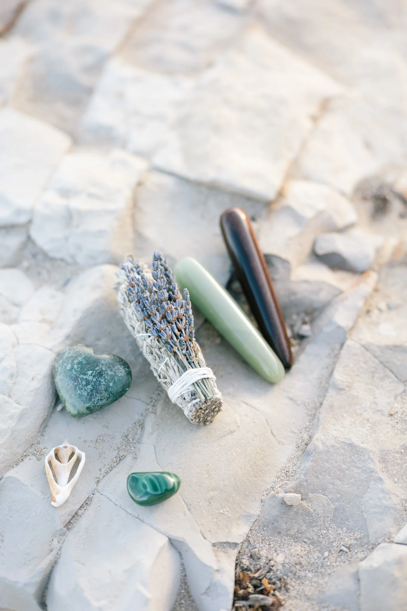 A collection of small rocks, shells, incense sticks, and crystals on a rocky surface.