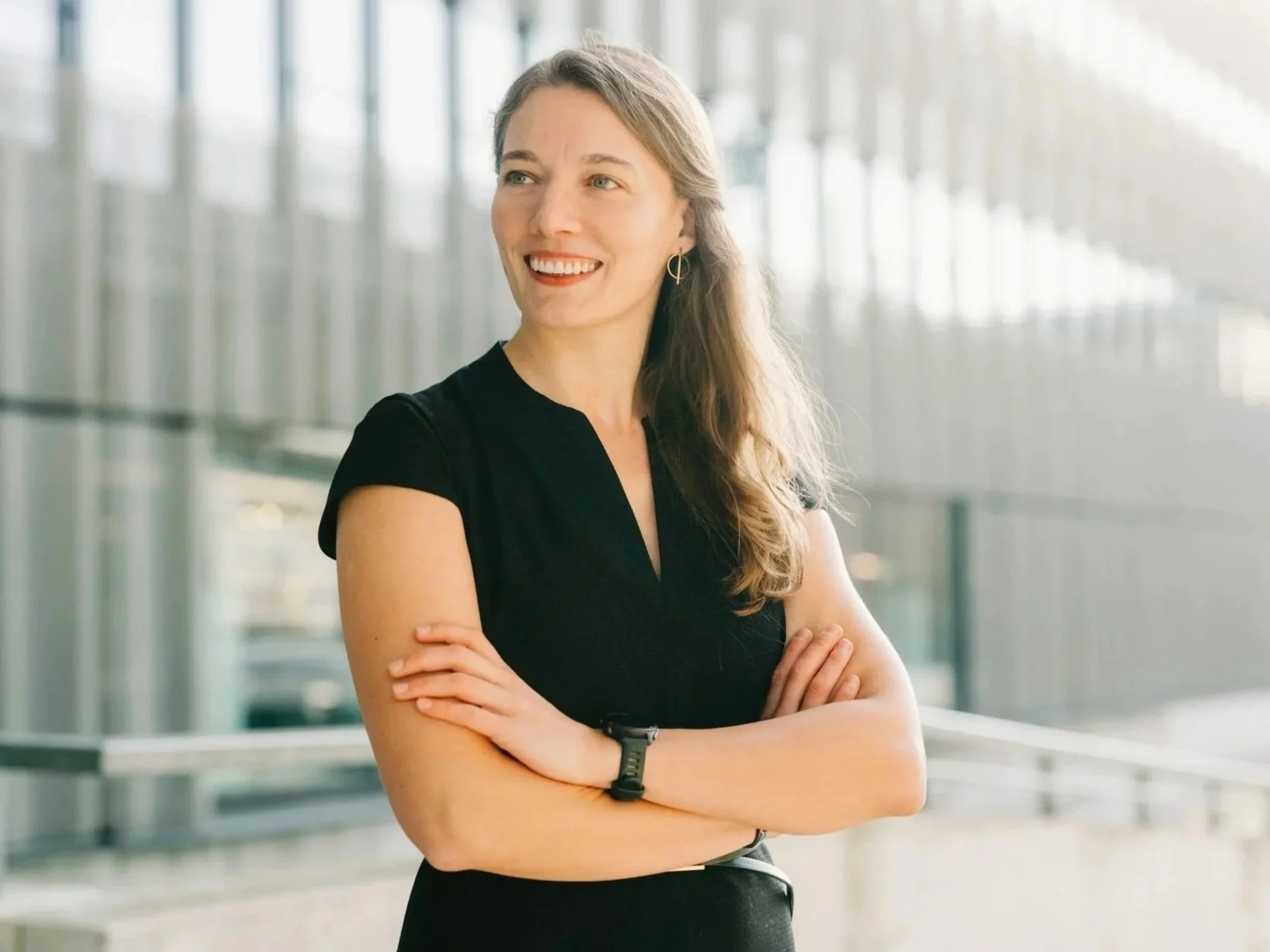 Smiling professional business woman with crossed arms standing in a bright modern office, ready to start coaching or consulting.
