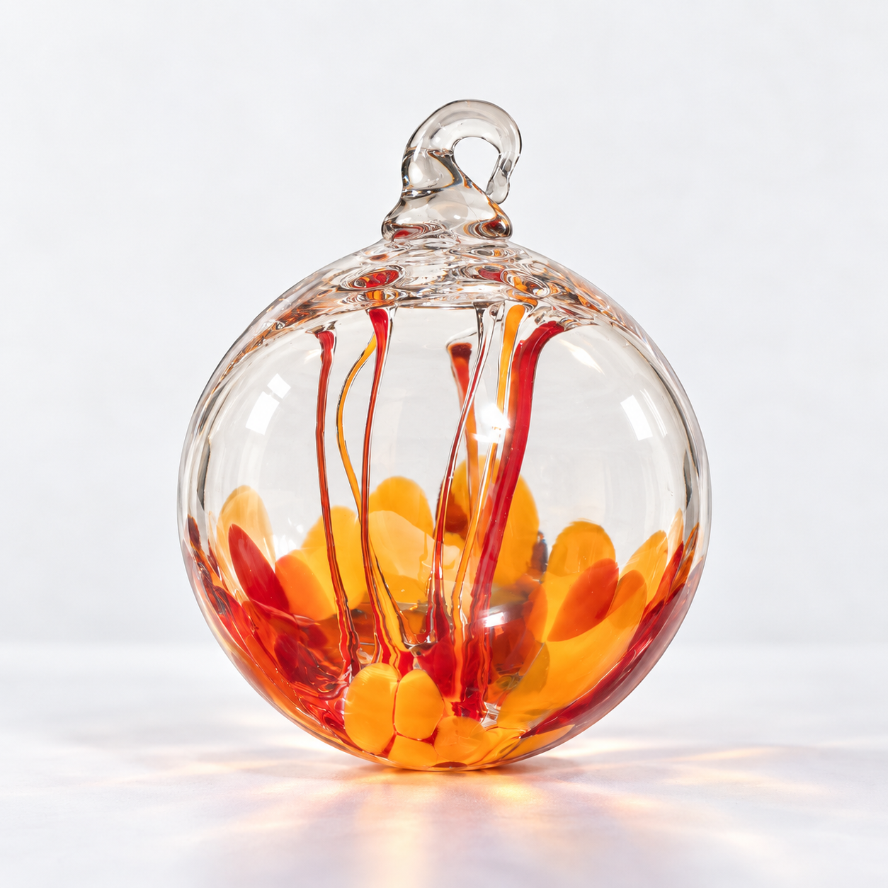 Glass ornament with orange and red glass pieces inside and red and orange streaks on the outside.
