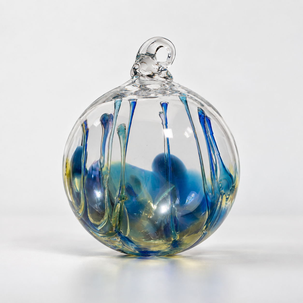 Glass sphere with colorful swirls and drips inside and on the surface, topped with a small loop, set against a plain white background.
