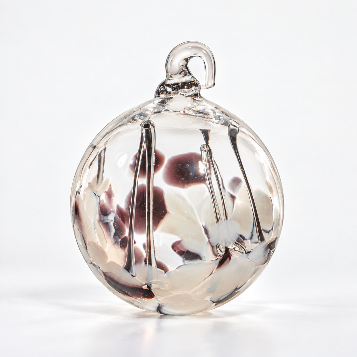 A clear glass ornament with a loop at the top, filled with abstract swirls and spots of white, black, and dark red colors.