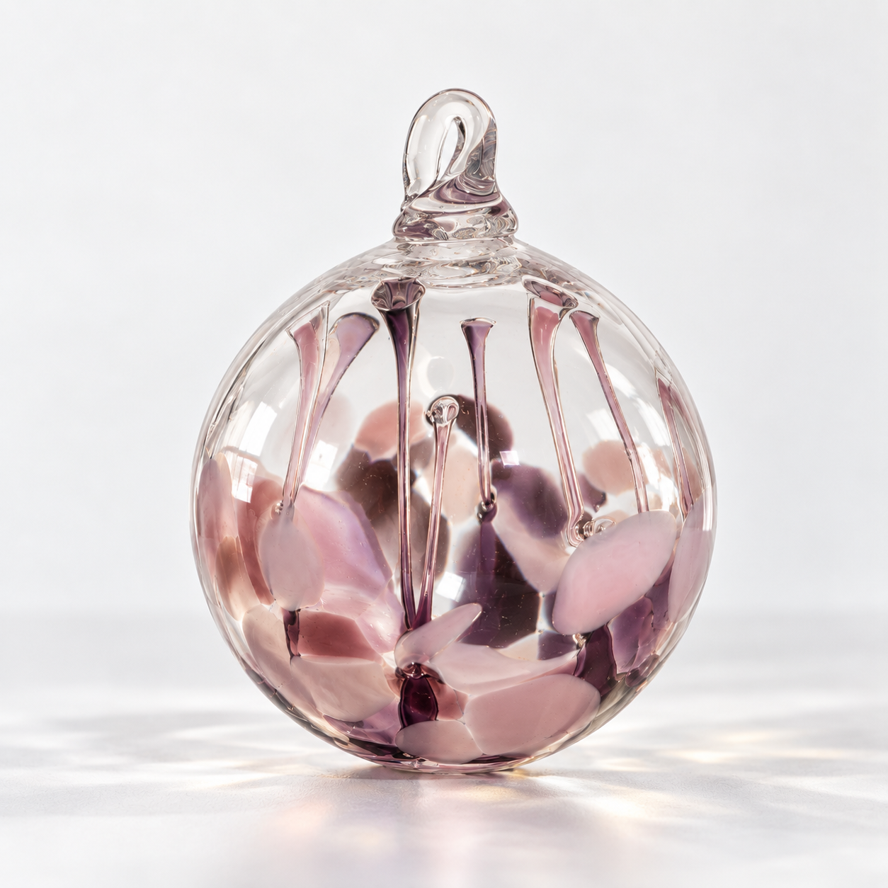 A clear glass decorative object with pink and purple abstract shapes inside, featuring a spherical shape with a loop at the top, against a white background.