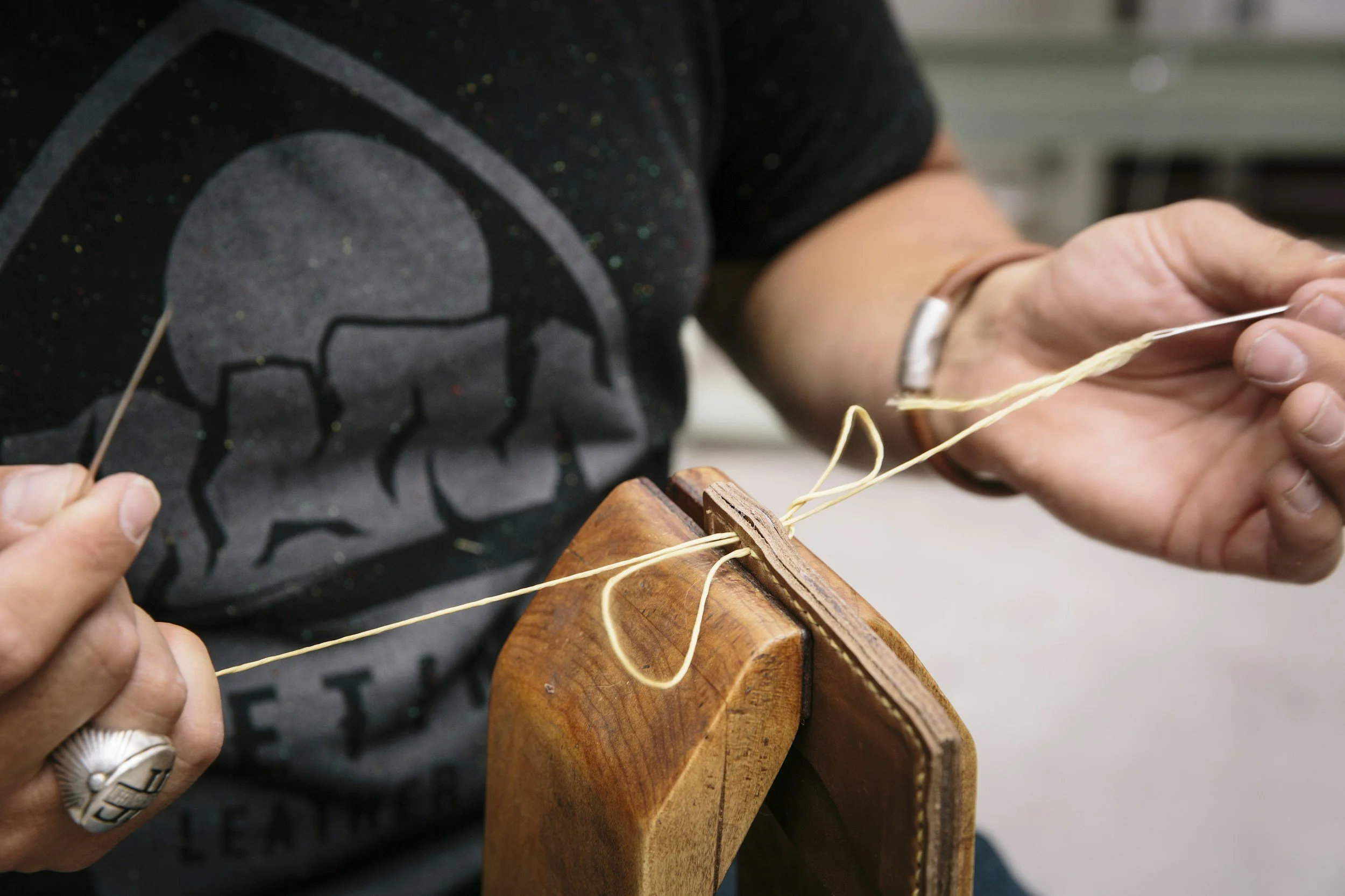 Hands stitching a leather piece by hand.