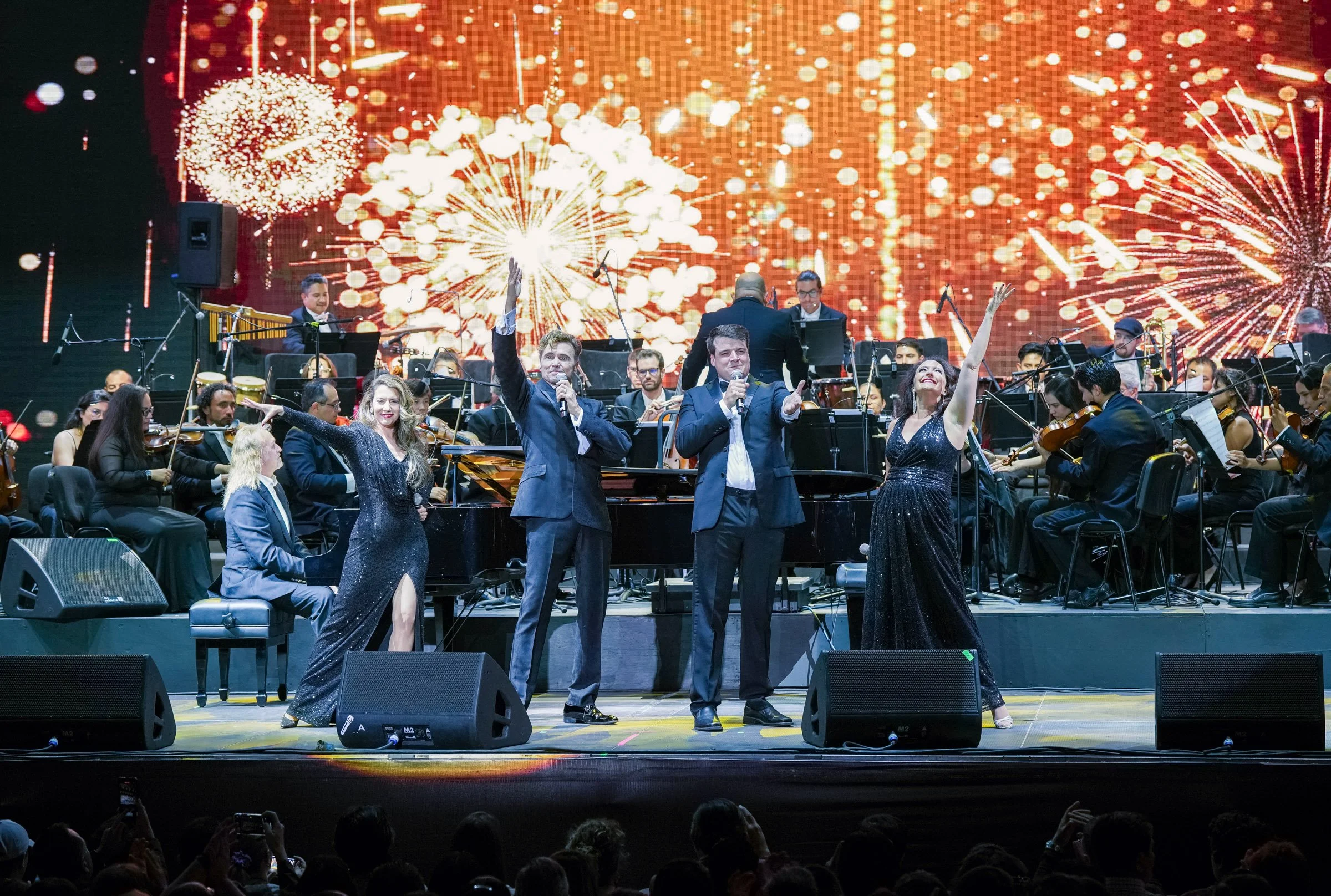 Orchestra performing on stage with a backdrop of fireworks display.