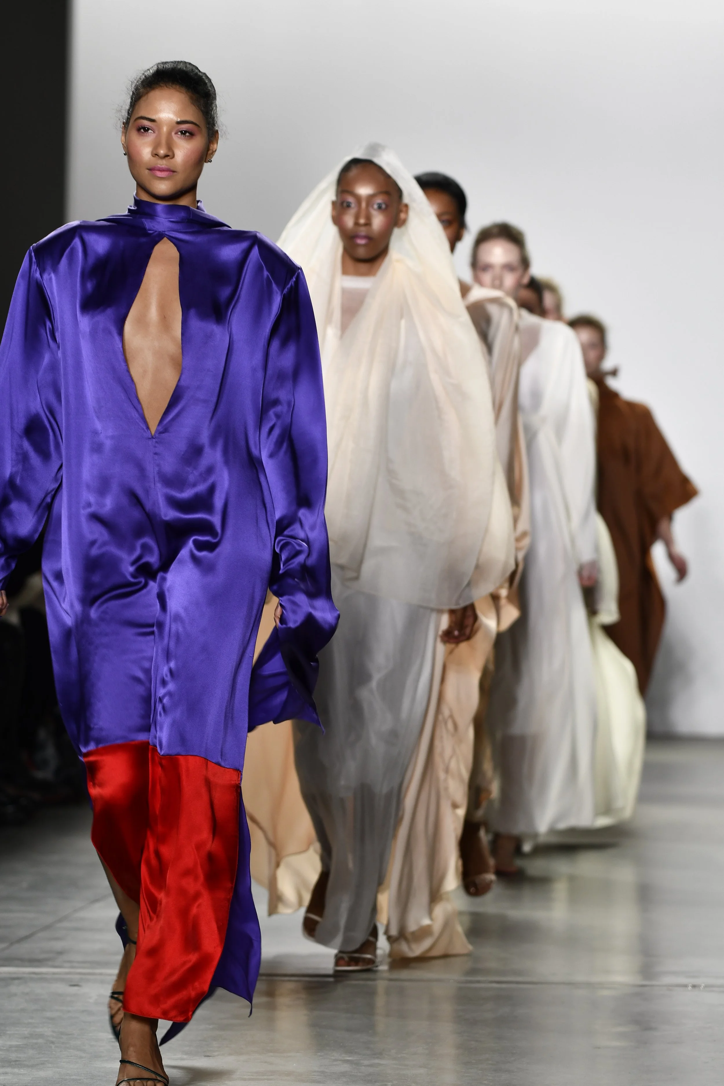 Models walking on a runway during a fashion show, wearing vibrant, colorful outfits.