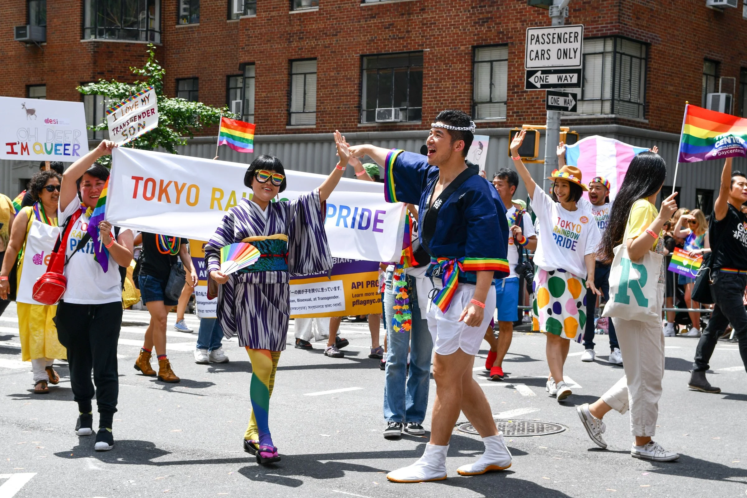 People participating in a pride parade wearing rainbow-themed clothing and accessories, holding rainbow flags and banners, celebrating LGBTQ+ pride on a city street at NY Pride Parade.
