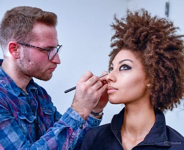Makeup artist applying makeup to a woman's face in a studio setting.