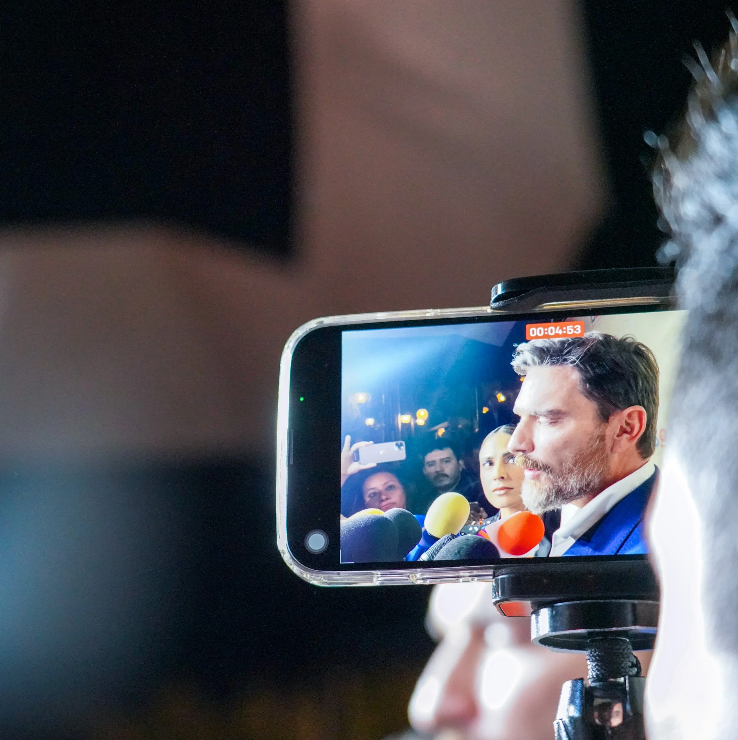 A smartphone on a table displaying a video call with multiple people, with the main person visible in the lower part of the screen, surrounded by other participants' faces. The image is viewed upside down.