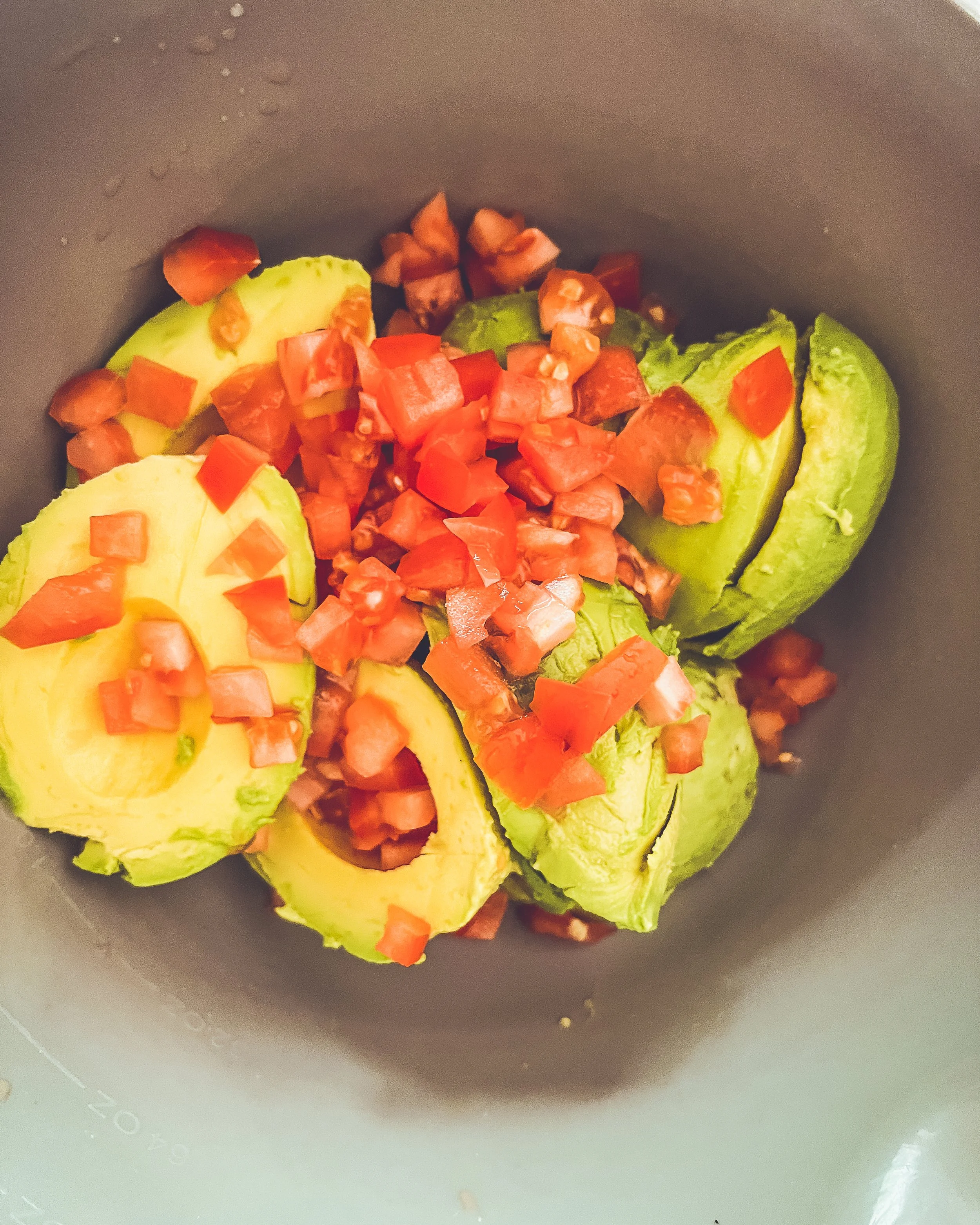 Sliced avocado topped with chopped red tomatoes in a gray bowl.