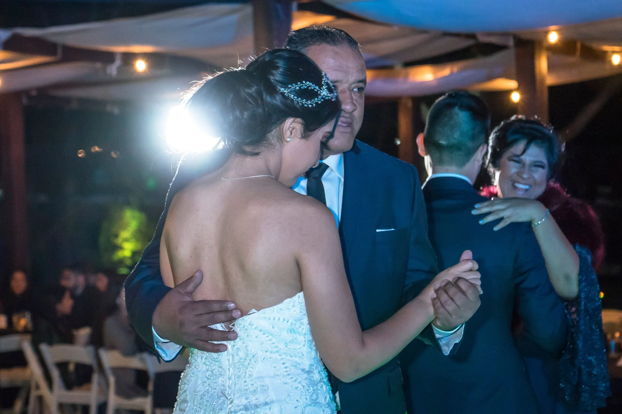 A couple dancing closely at an indoor event during the evening, with other guests in the background.
