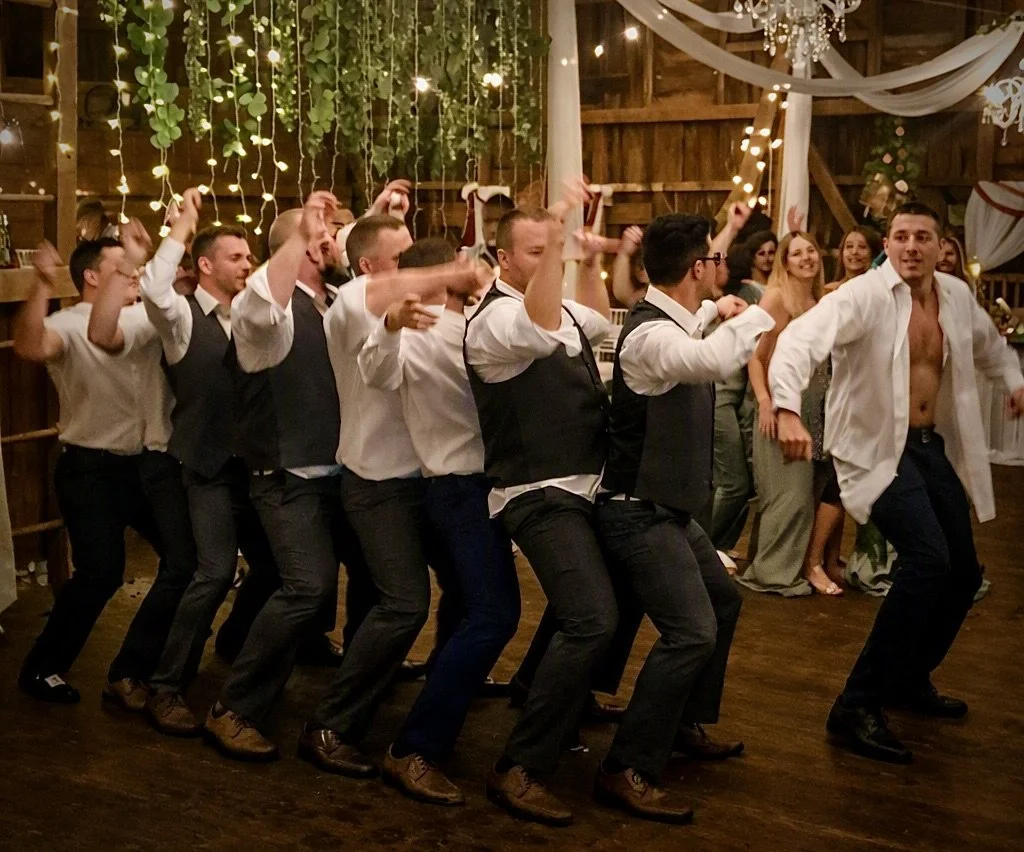 Group of men in formal attire dancing and having fun at a wedding reception or party.