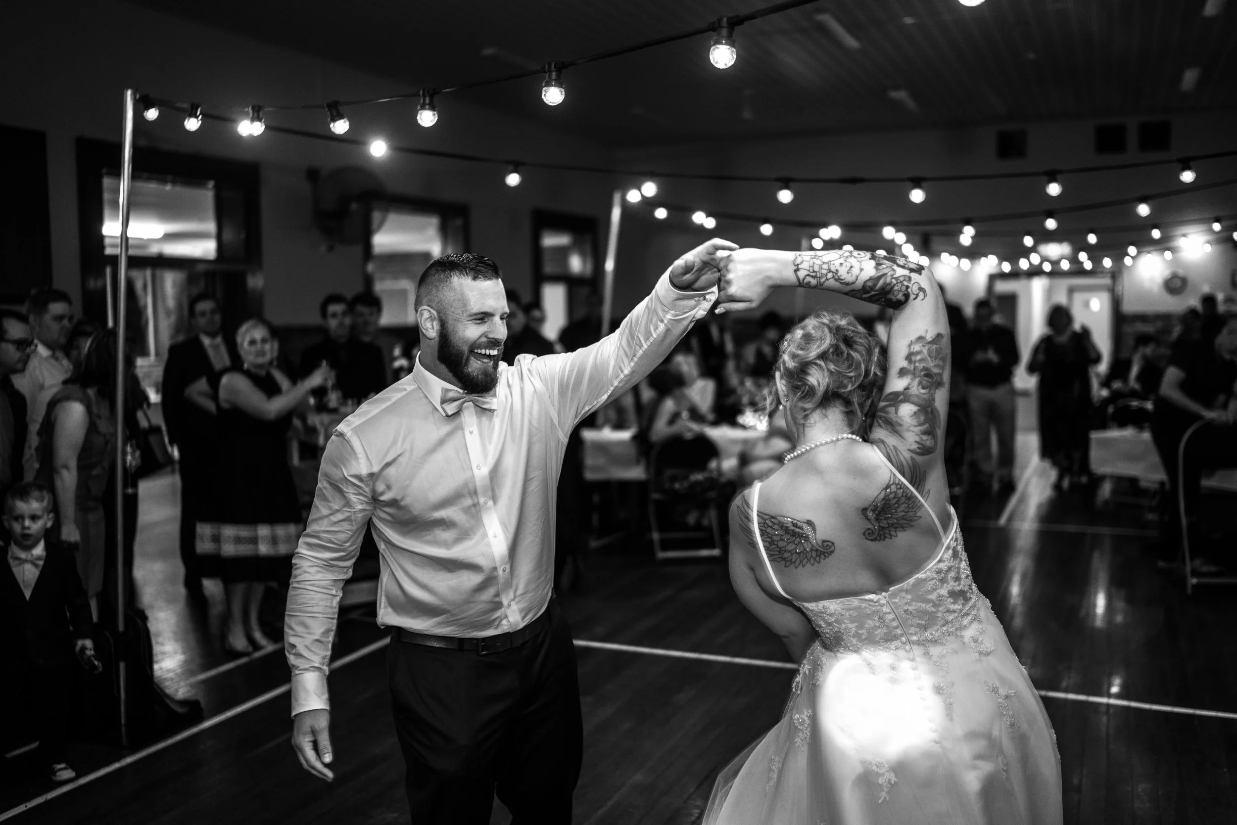 A groom and bride dancing at their wedding reception, surrounded by guests and string lights.