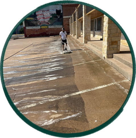 Person cleaning a concrete sidewalk outside a building with stone columns
