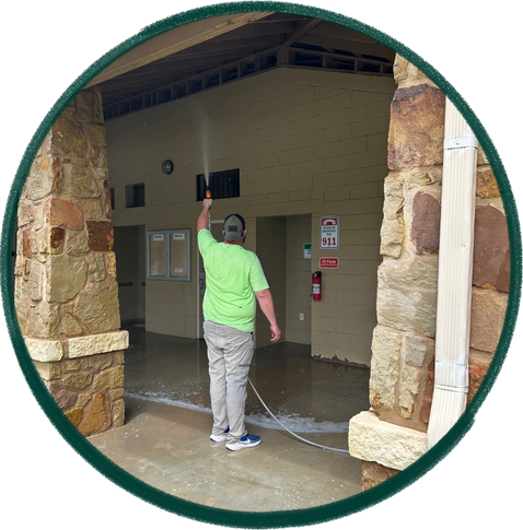 Man in a green shirt and gray pants spray washing a stone entrance archway.