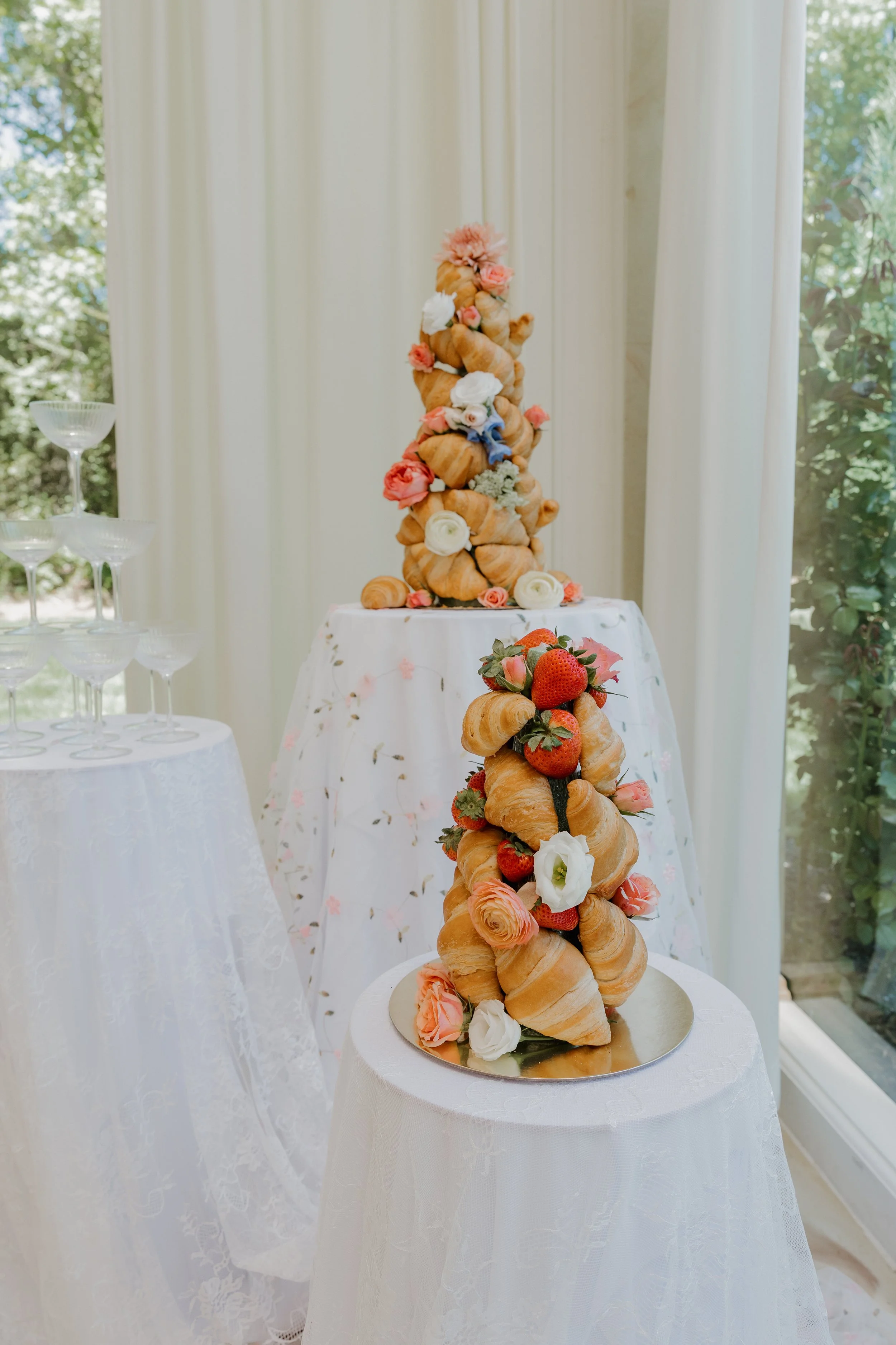 A tall wedding cake made of stacked croissants decorated with strawberries, roses, and other flowers, displayed on a table with a white tablecloth.