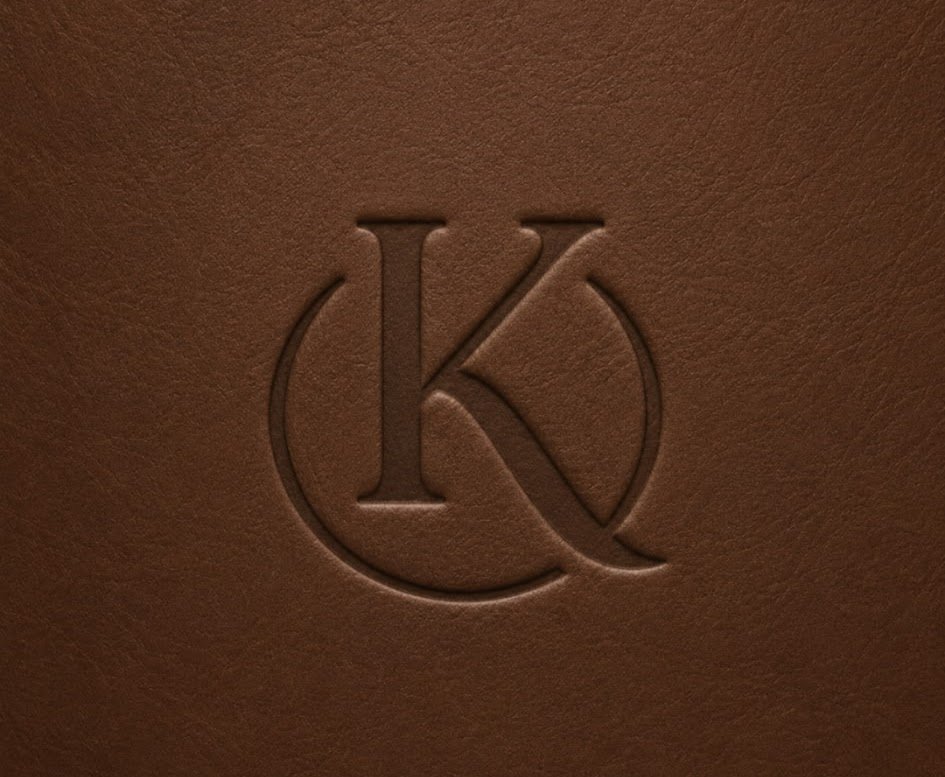 Close-up of a brown leather surface with an embossed logo featuring the letters K and C intertwined inside a circle.