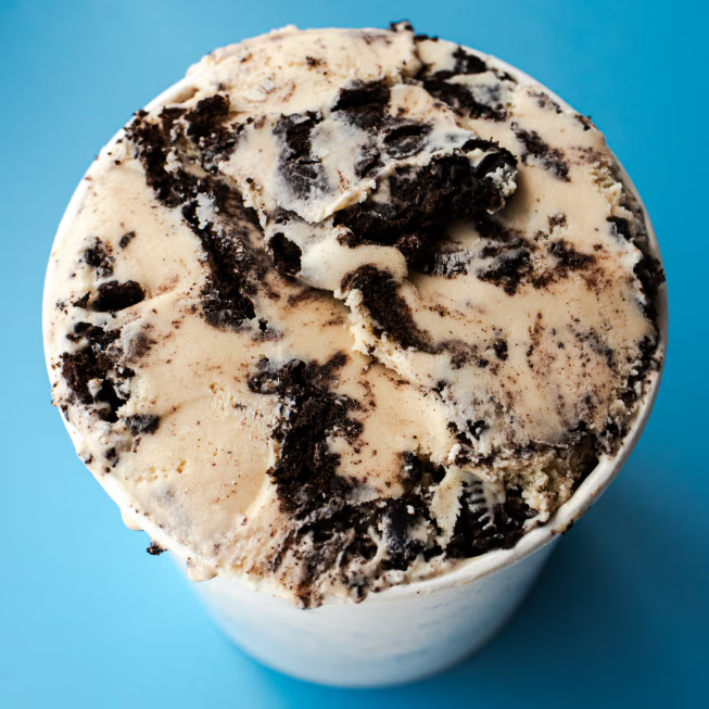 Close-up of a cup of cookies and cream ice cream with chocolate cookie chunks on a light blue background.