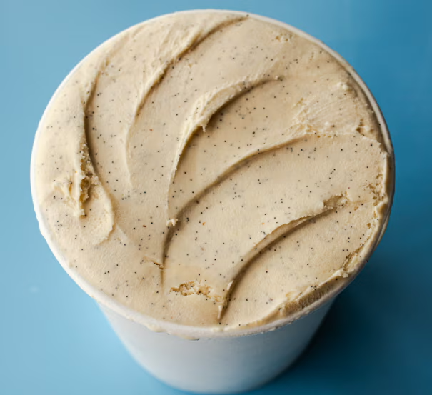 Close-up of a creamy, light-colored frozen dairy treat topped with black pepper, in a white cup against a blue background.