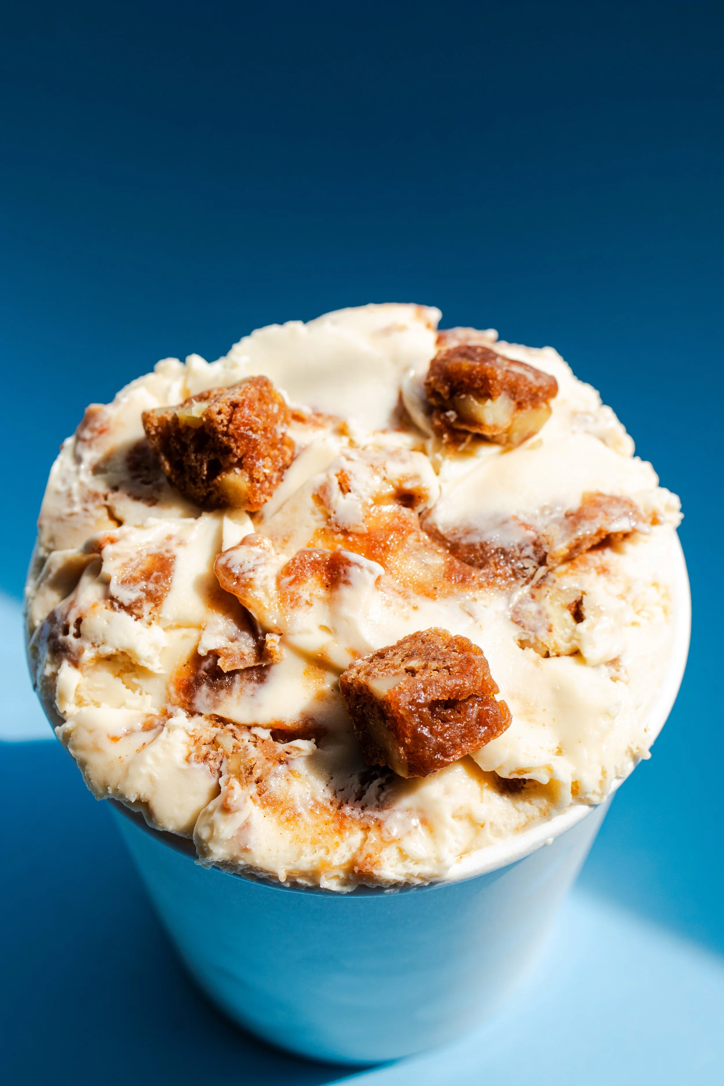 Close-up of a cup of birthday ice cream with caramel and chocolate toppings against a blue background.
