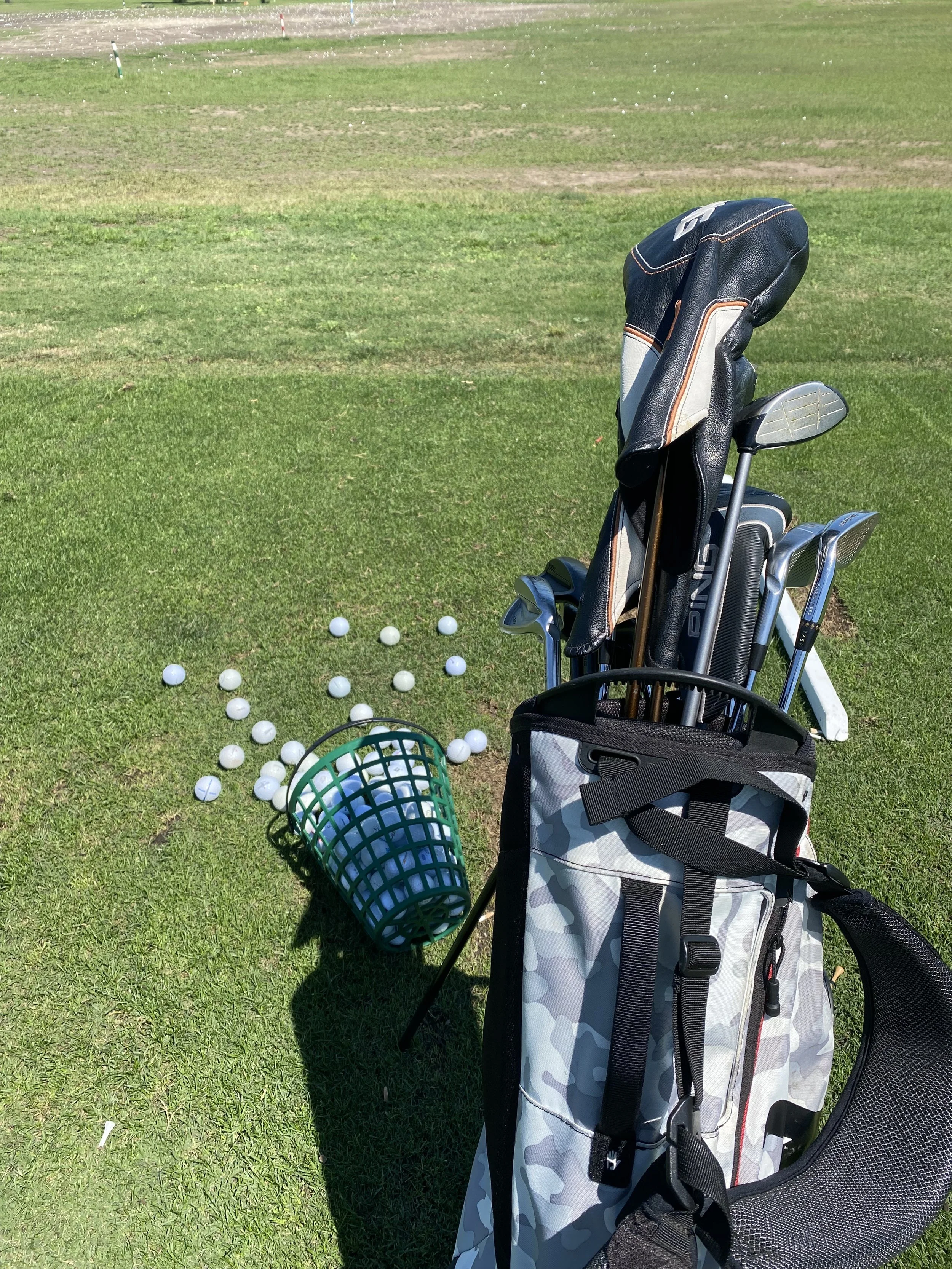 A golf bag with golf clubs standing on a green golf course with a golf net and scattered golf balls nearby.