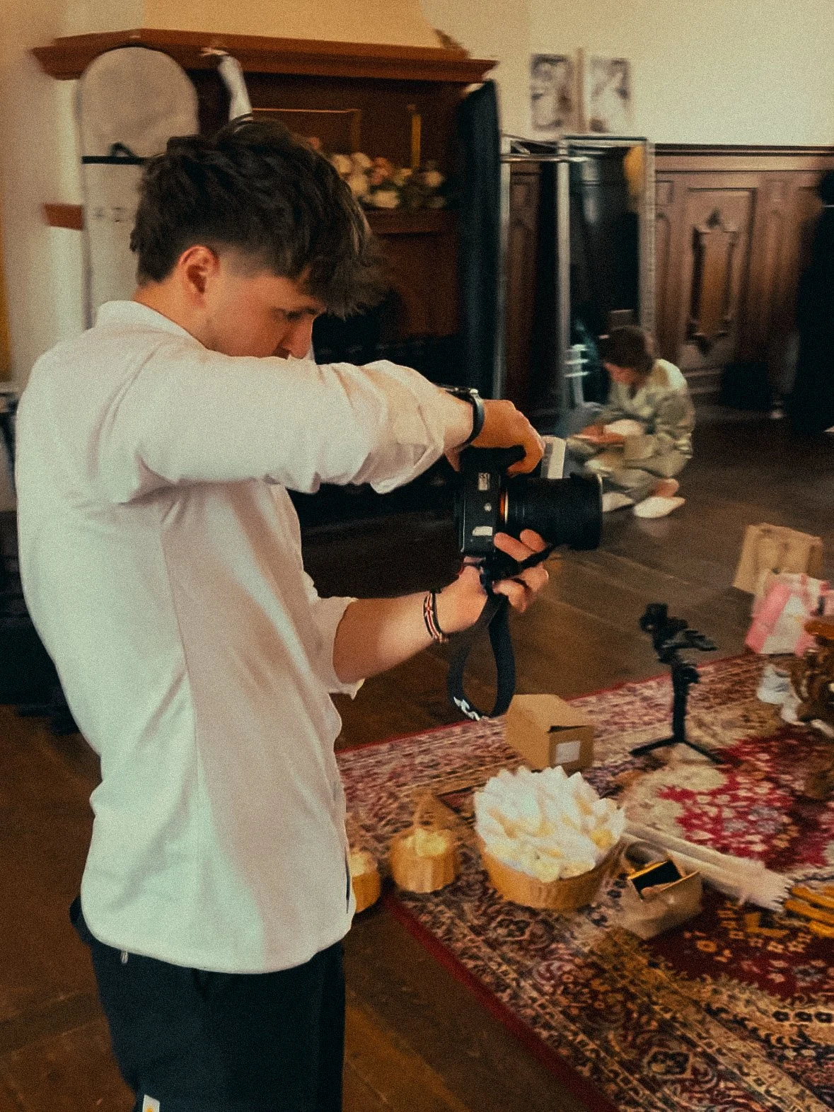 Junge fotografiert im Wohnzimmer mit Kamera, im Hintergrund Kind auf dem Boden, zur Dekoration Tortenbrände auf dem Tisch.