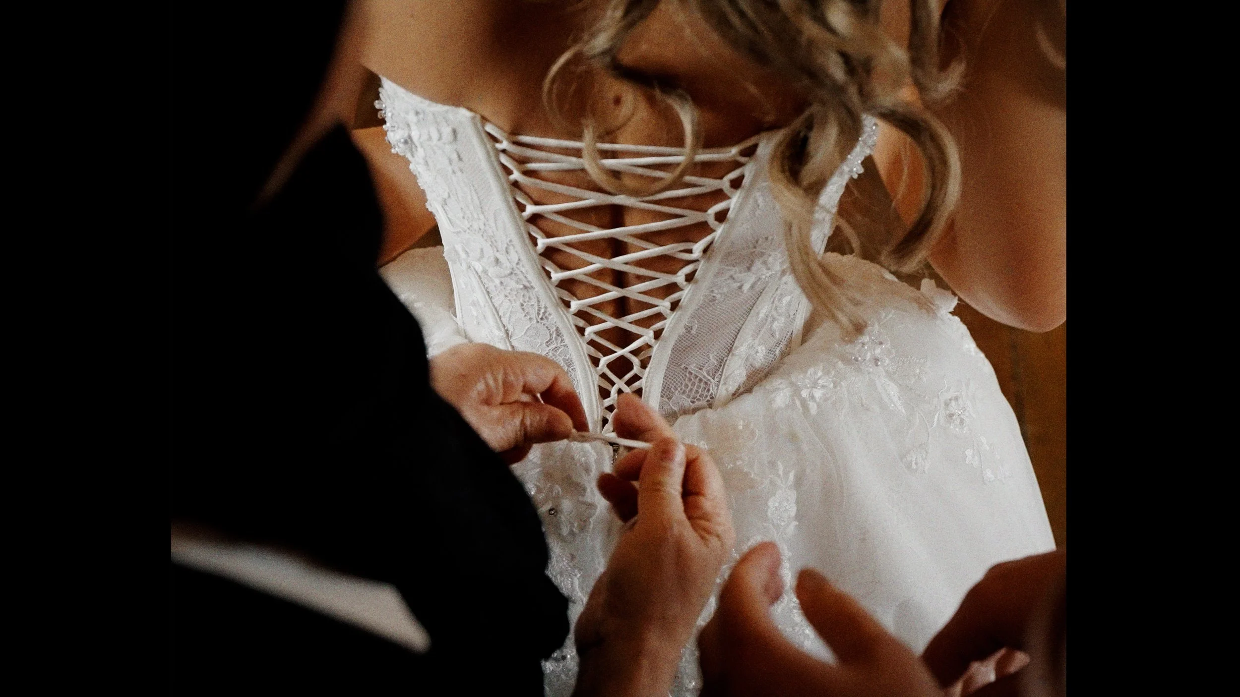 Nahaufnahme einer Braut, die einen weißen, verzierte Hochzeitskleid trägt, während jemand das Kleid oder die Schnürung richtet.