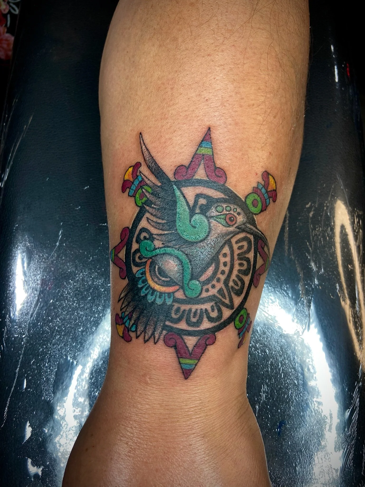 Colorful tattoo of a clock with wings, surrounded by decorative elements, on a person's arm.