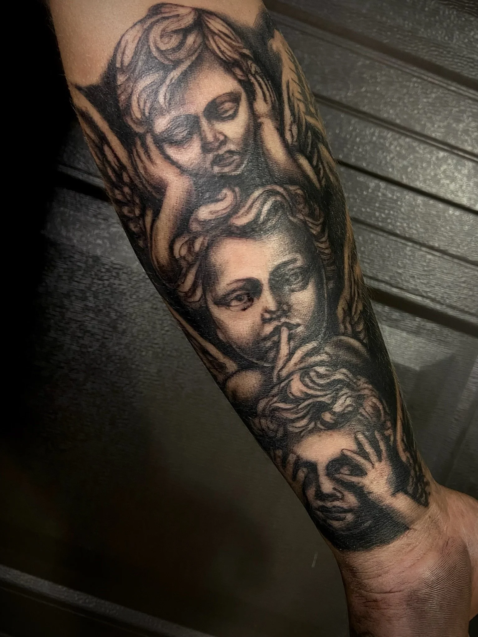 Tattoo on an arm depicting two women with detailed facial features and flowing hair, rendered in black and gray ink.