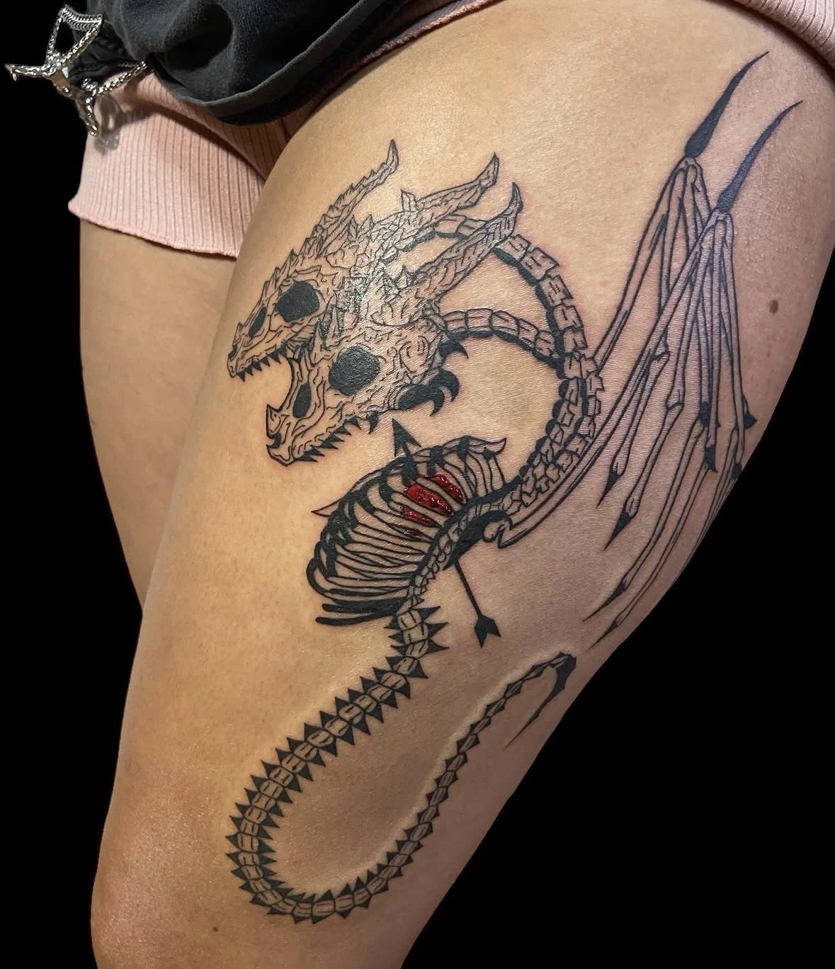 Tattoo of a dragon skull with detailed line work, large eye sockets, and sharp teeth, with its neck and body coiled around the arm, featuring extended wings and a long, pointed tail by tattoo artist Agua at Floating Streams Tattoo.